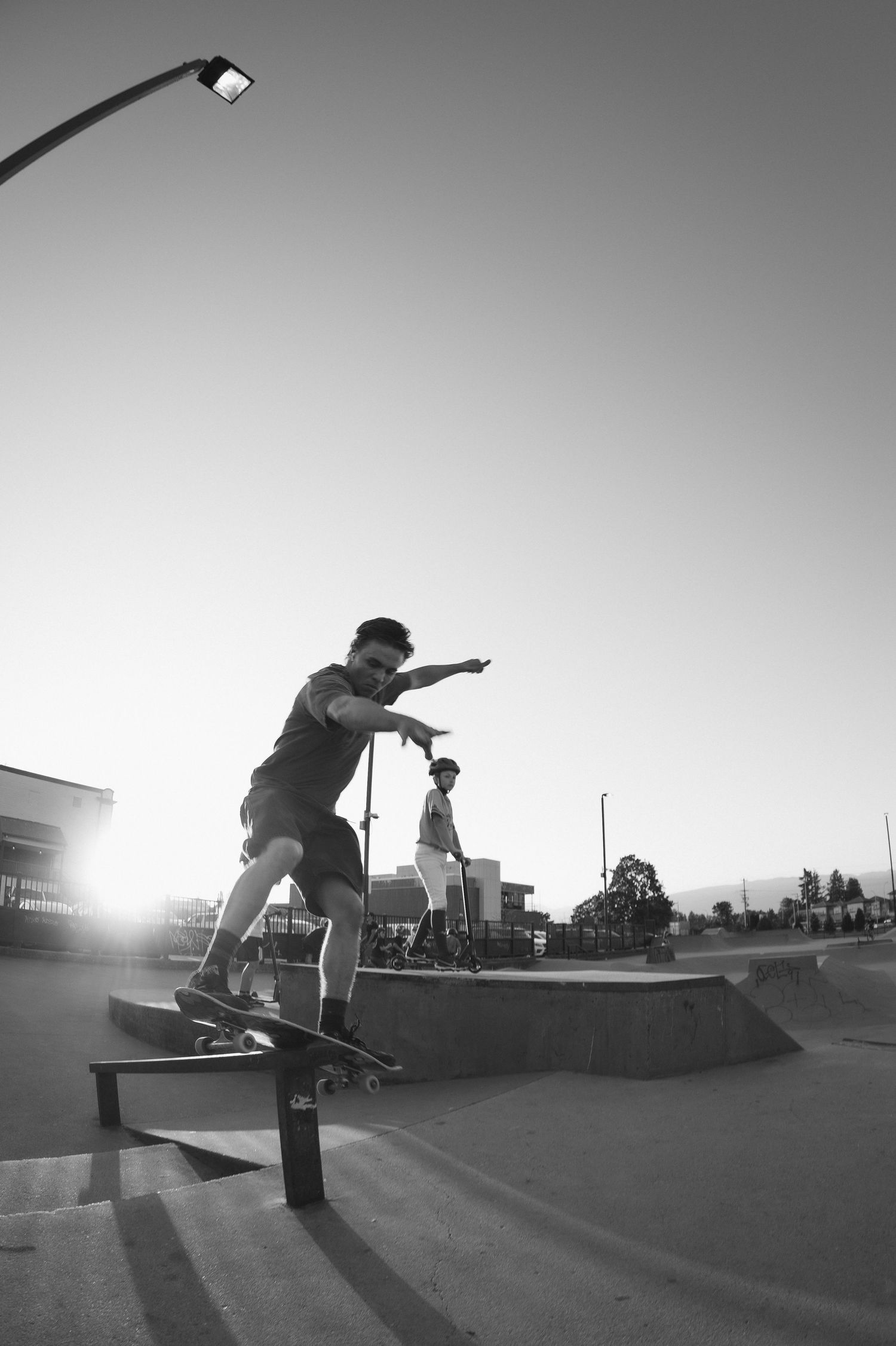 Black and white photo of skateboarder grinding a rail at a skate park with sun flare.