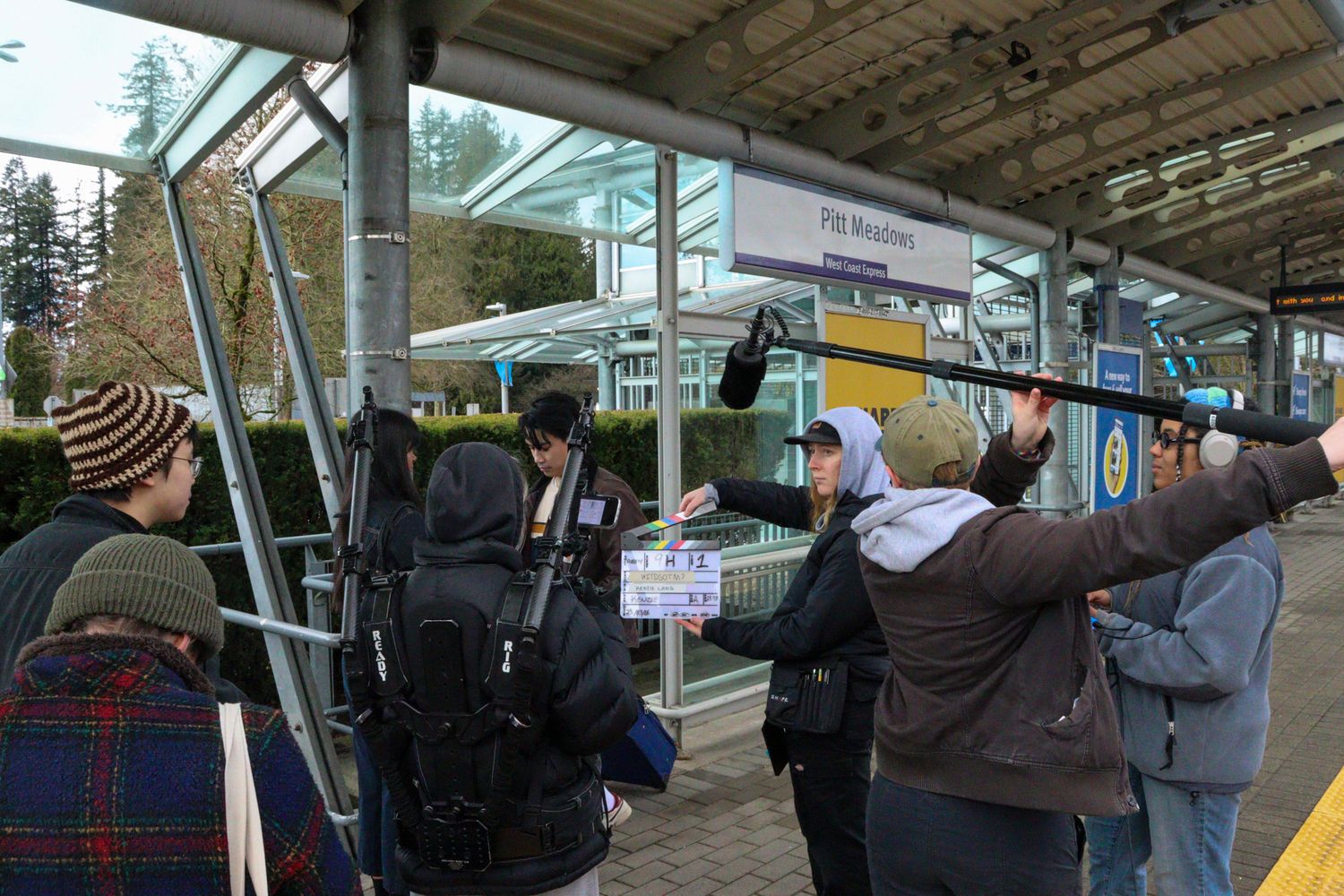 Film crew with clapperboard and boom mic shooting at Pitt Meadows station.