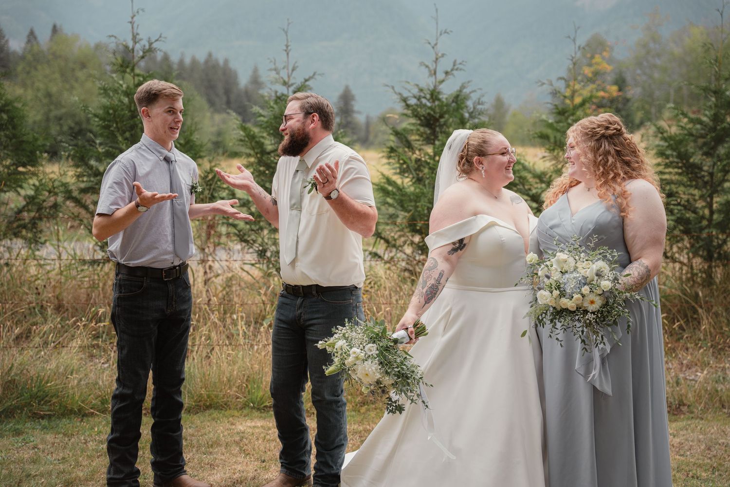 Groom gestures while speaking to young man as bride and bridesmaid look on outdoors.