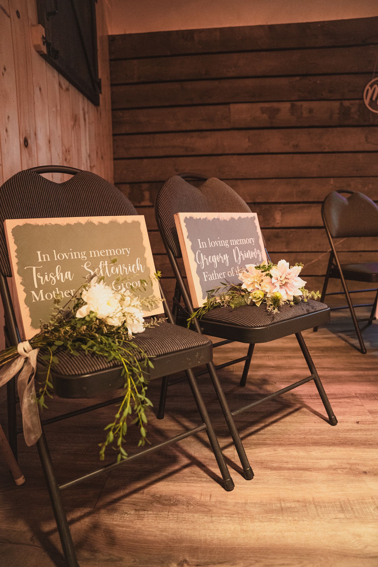 Two memorial chairs with floral arrangements and in loving memory signs honoring deceased family members at a wedding.