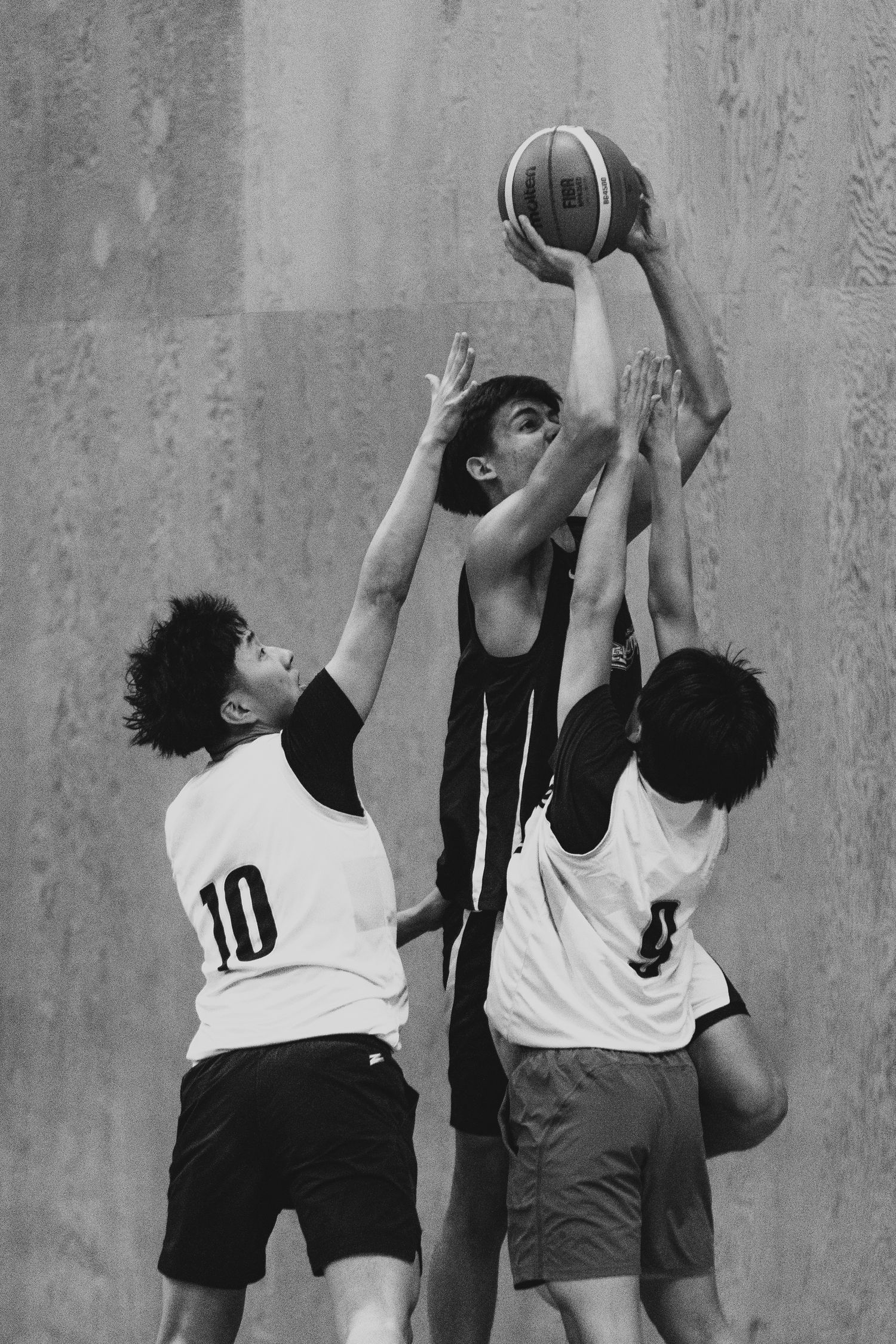 Three basketball players battle for the ball during an intense indoor game, player 10 visible.