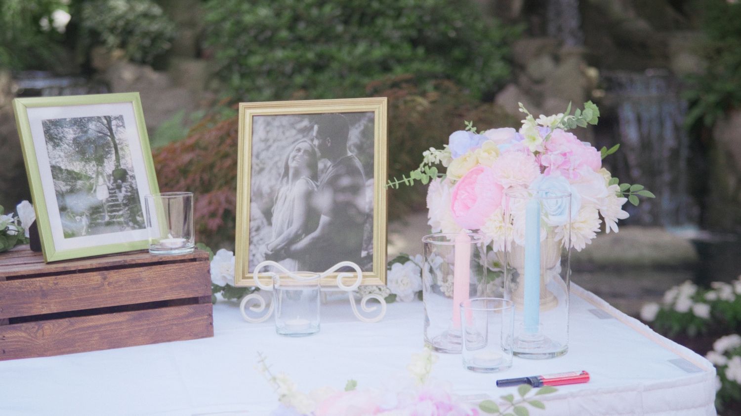 Elegant wedding reception table with pink floral arrangement, vintage photo frames, and decorative items on white tablecloth.