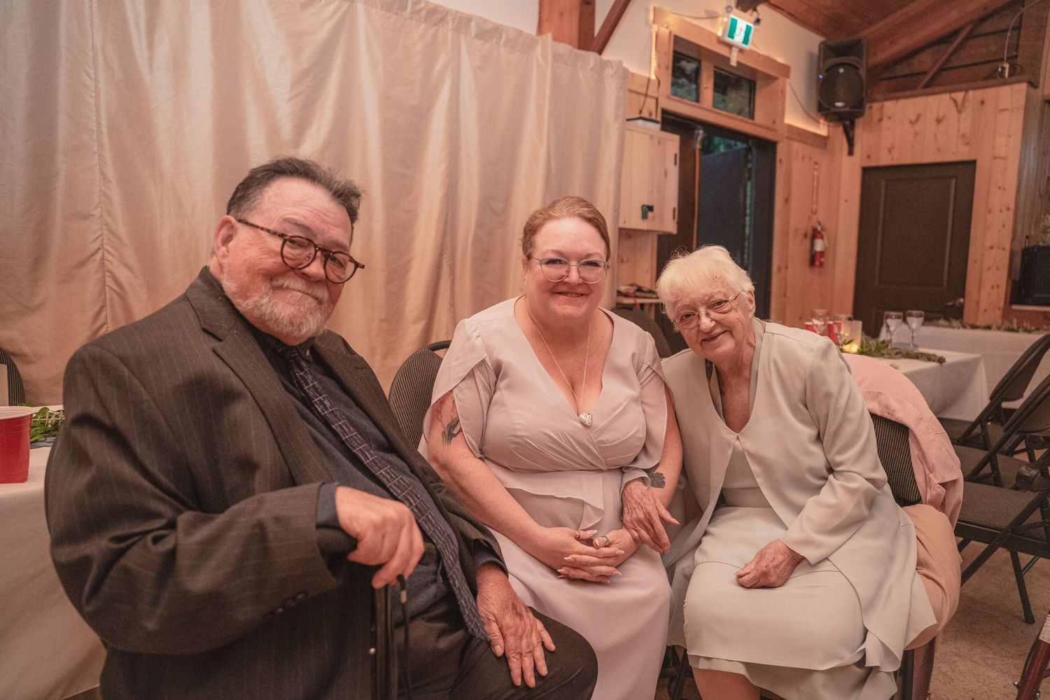 Three wedding guests pose together smiling at a warmly lit rustic barn reception venue.