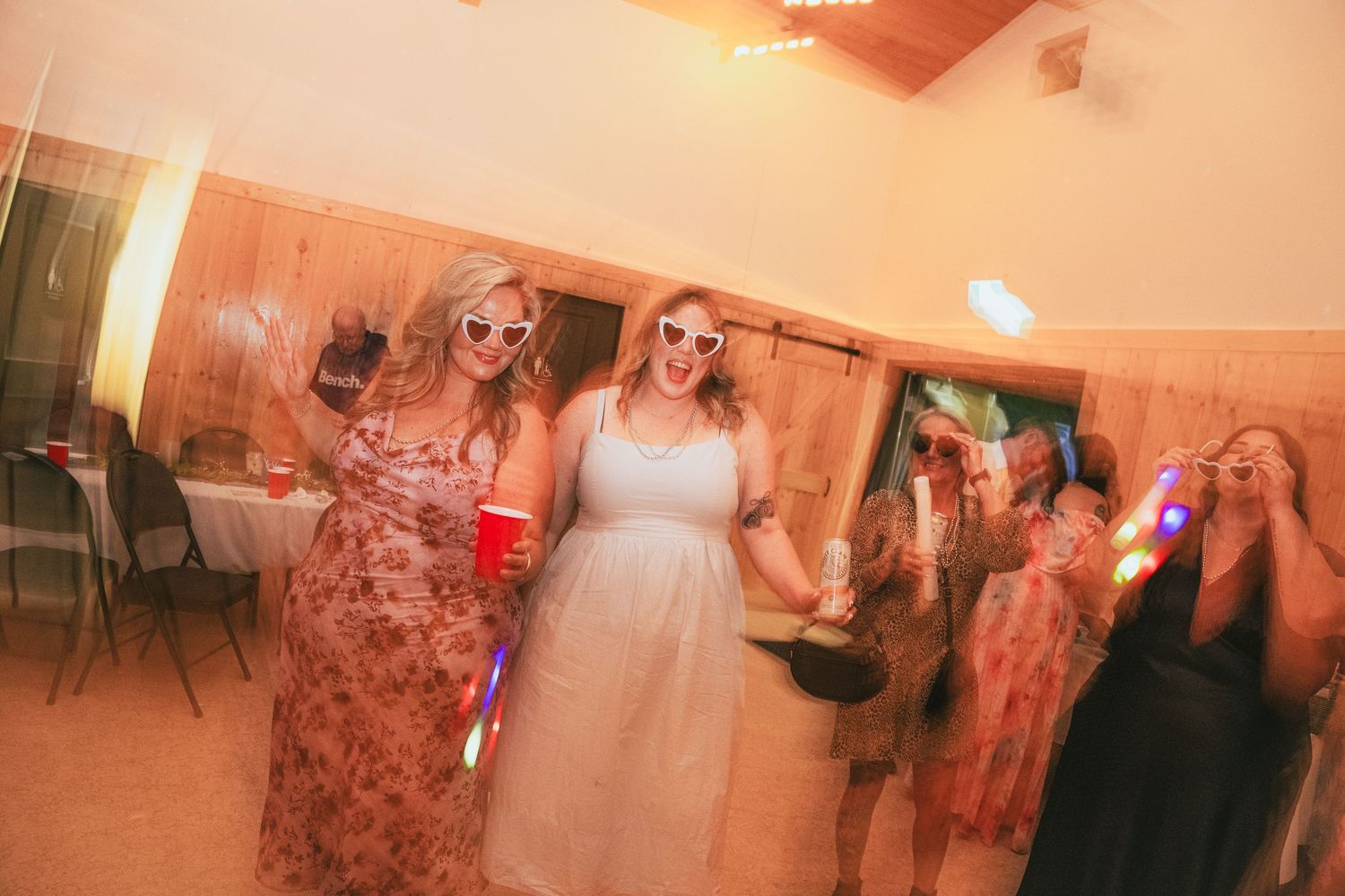 Bride in white dress dancing with guests wearing sunglasses at a lively wedding reception party.