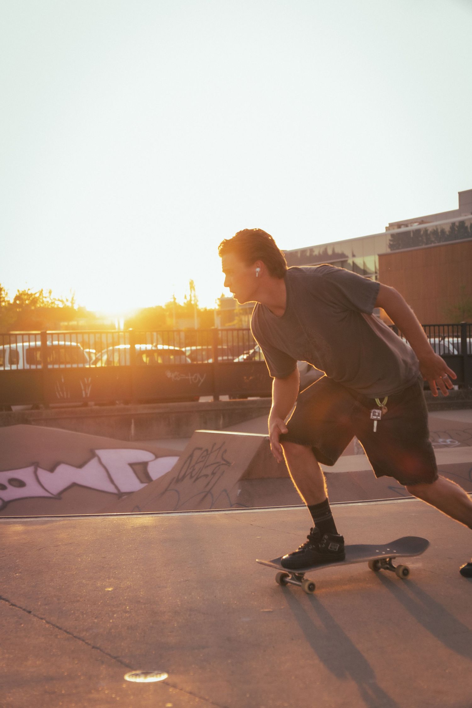 Young man skateboarding at an outdoor skate park bathed in warm golden sunset light.