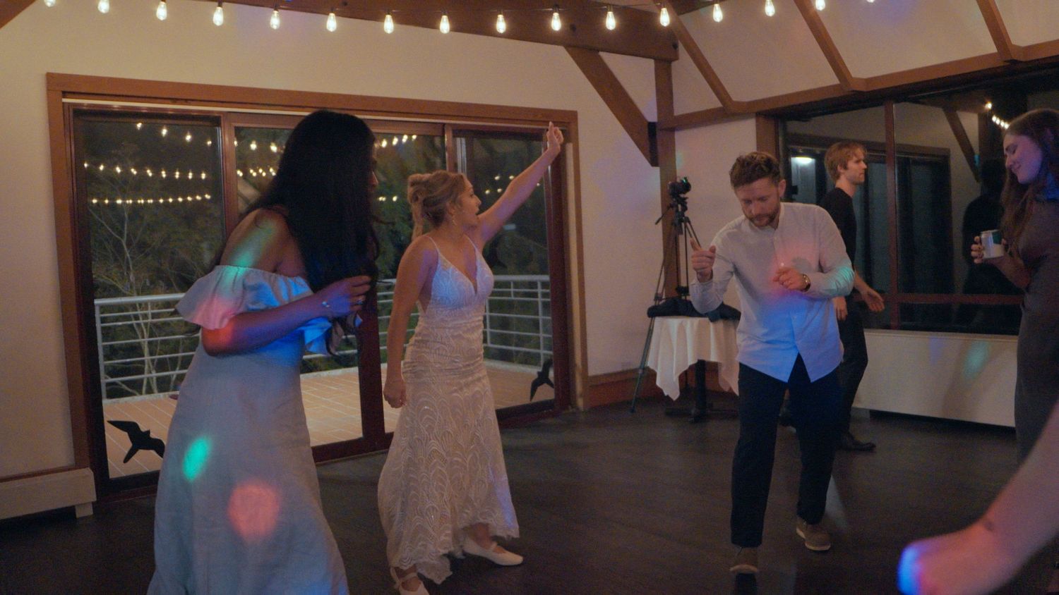 Guests dancing under colorful disco lights at a lively wedding reception in a rustic barn venue.