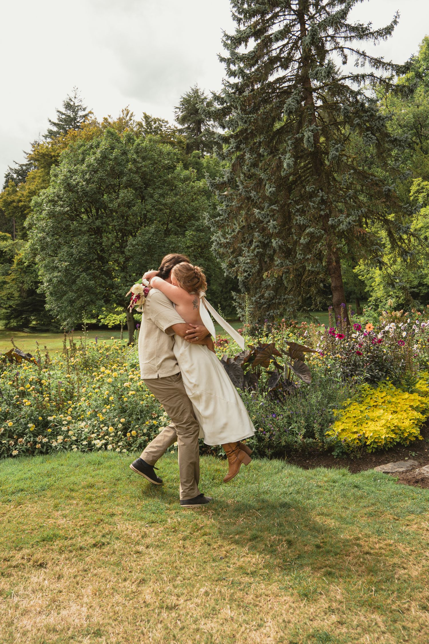 Bride and groom sharing a romantic lift and embrace in a beautiful garden with colorful blooms.