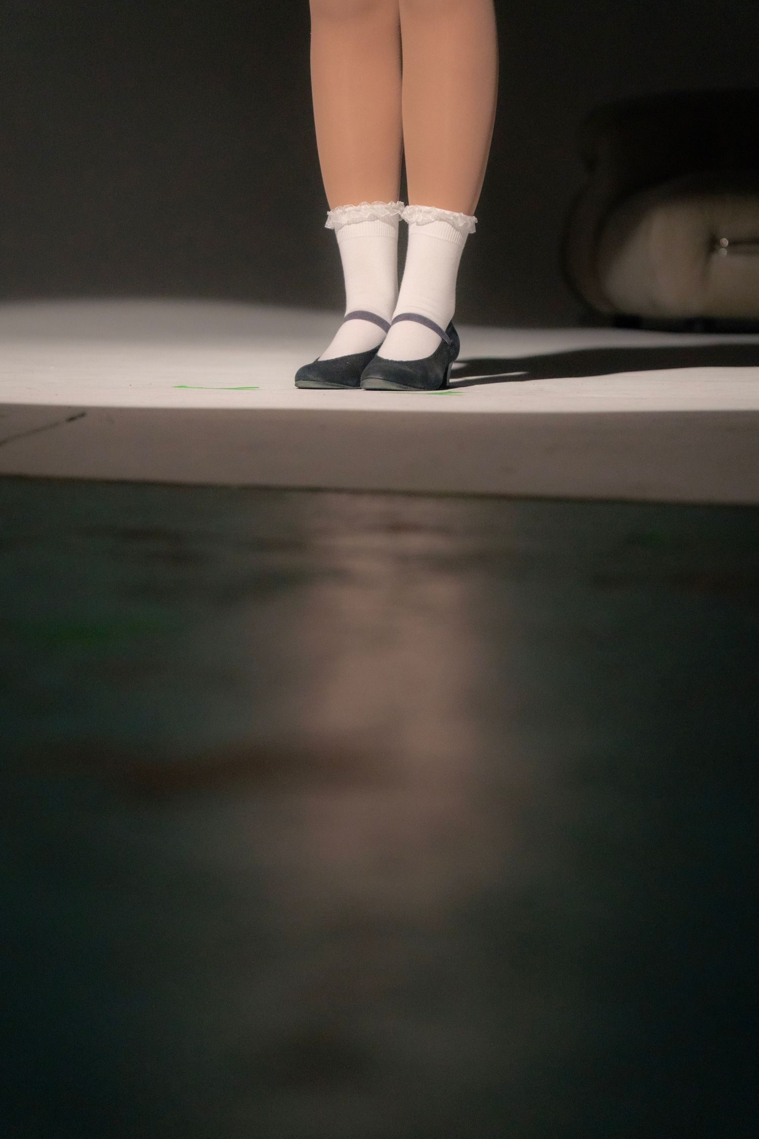 Child's legs in white lace socks and black Mary Jane shoes standing on a stage under spotlight.