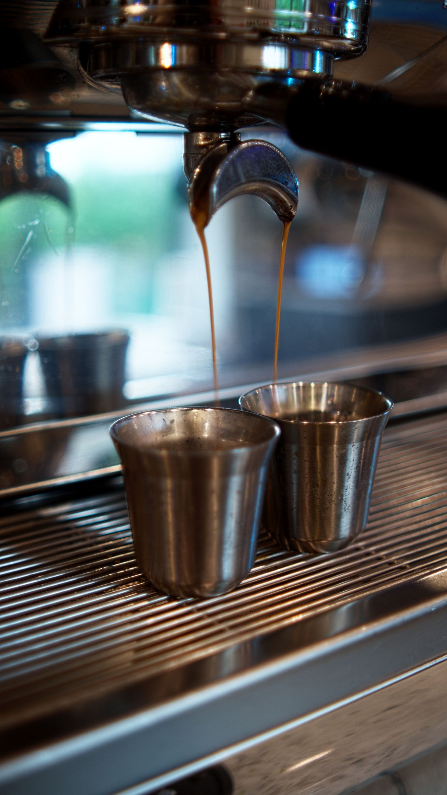 Professional espresso machine extracting rich crema coffee into two shiny stainless steel cups.