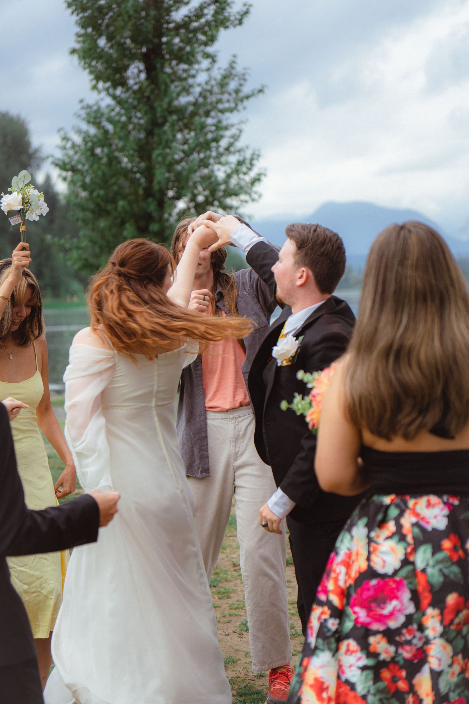 Bride and groom dancing joyfully with wedding guests celebrating outdoors with mountain backdrop.