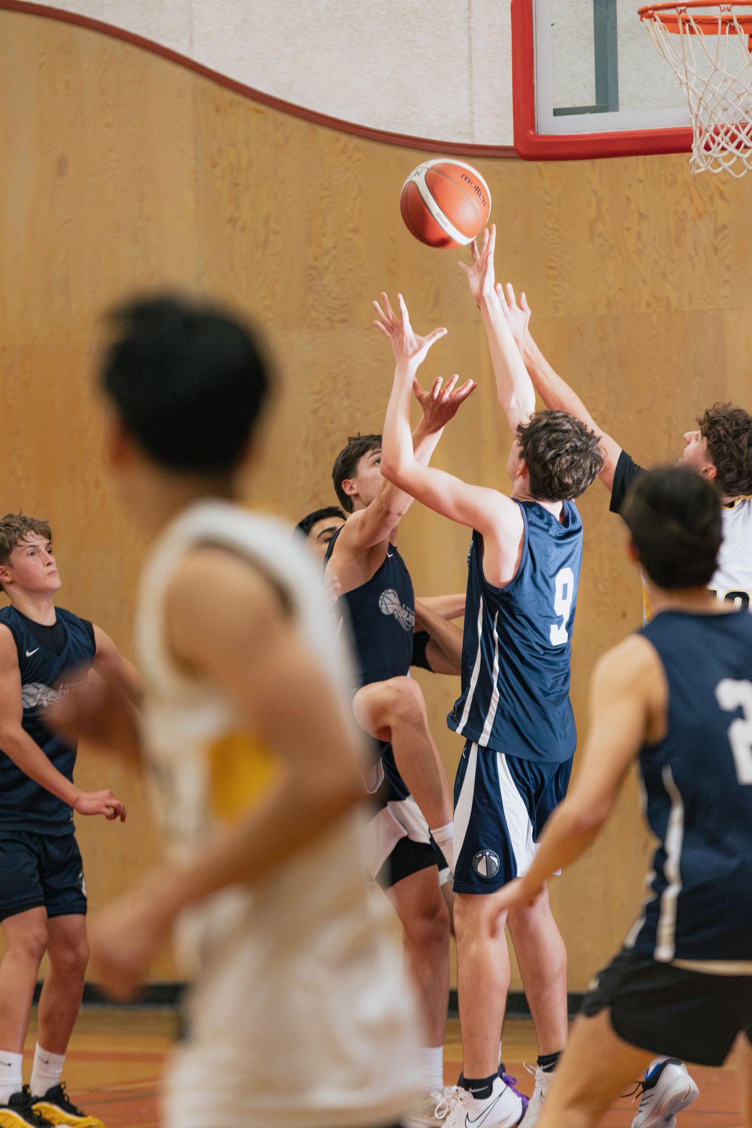 Young basketball players in blue uniforms compete for the ball during an indoor gymnasium game.