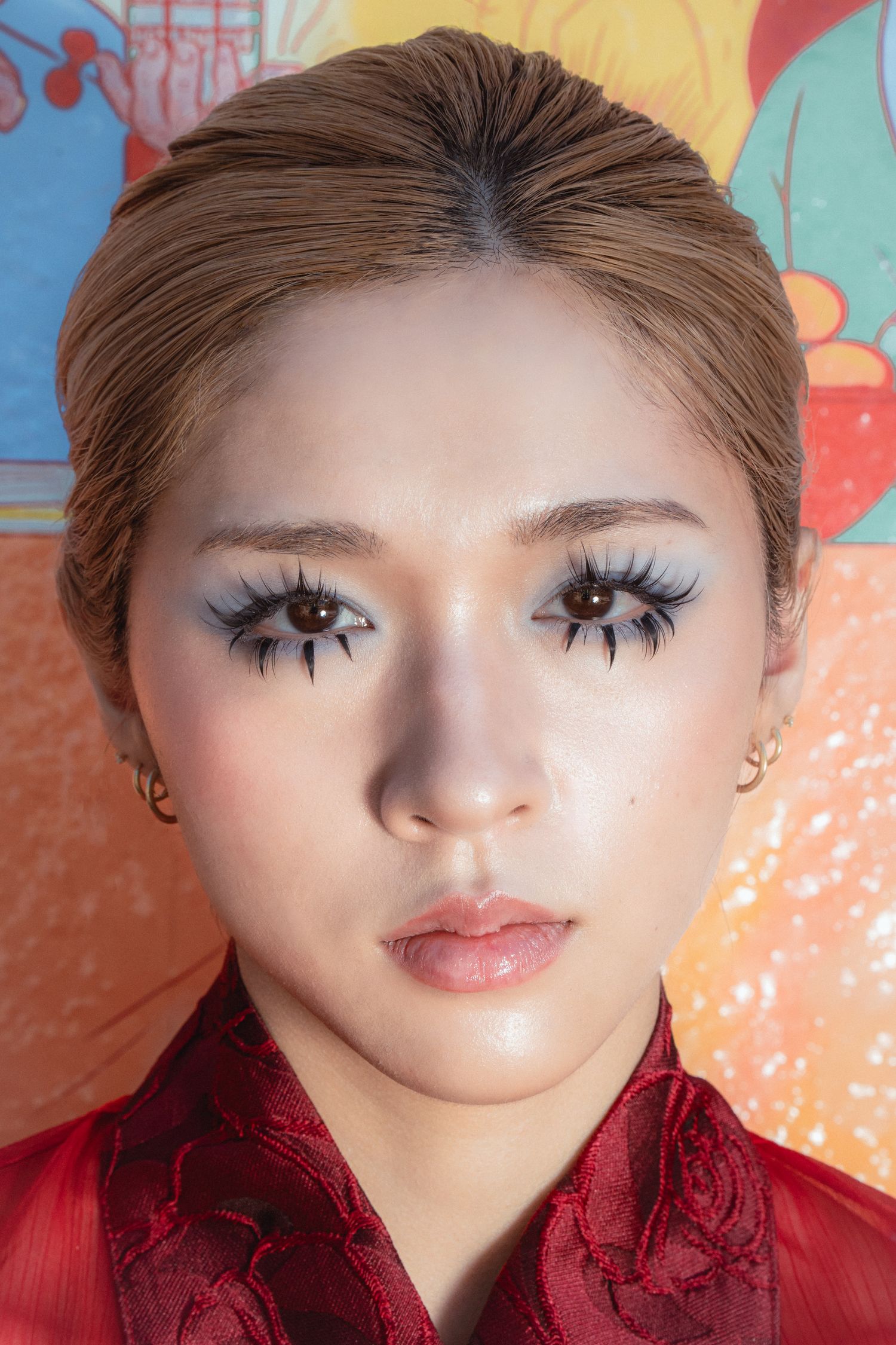 Young Asian woman with dramatic false eyelashes and white eyeshadow wearing a red traditional Chinese outfit.