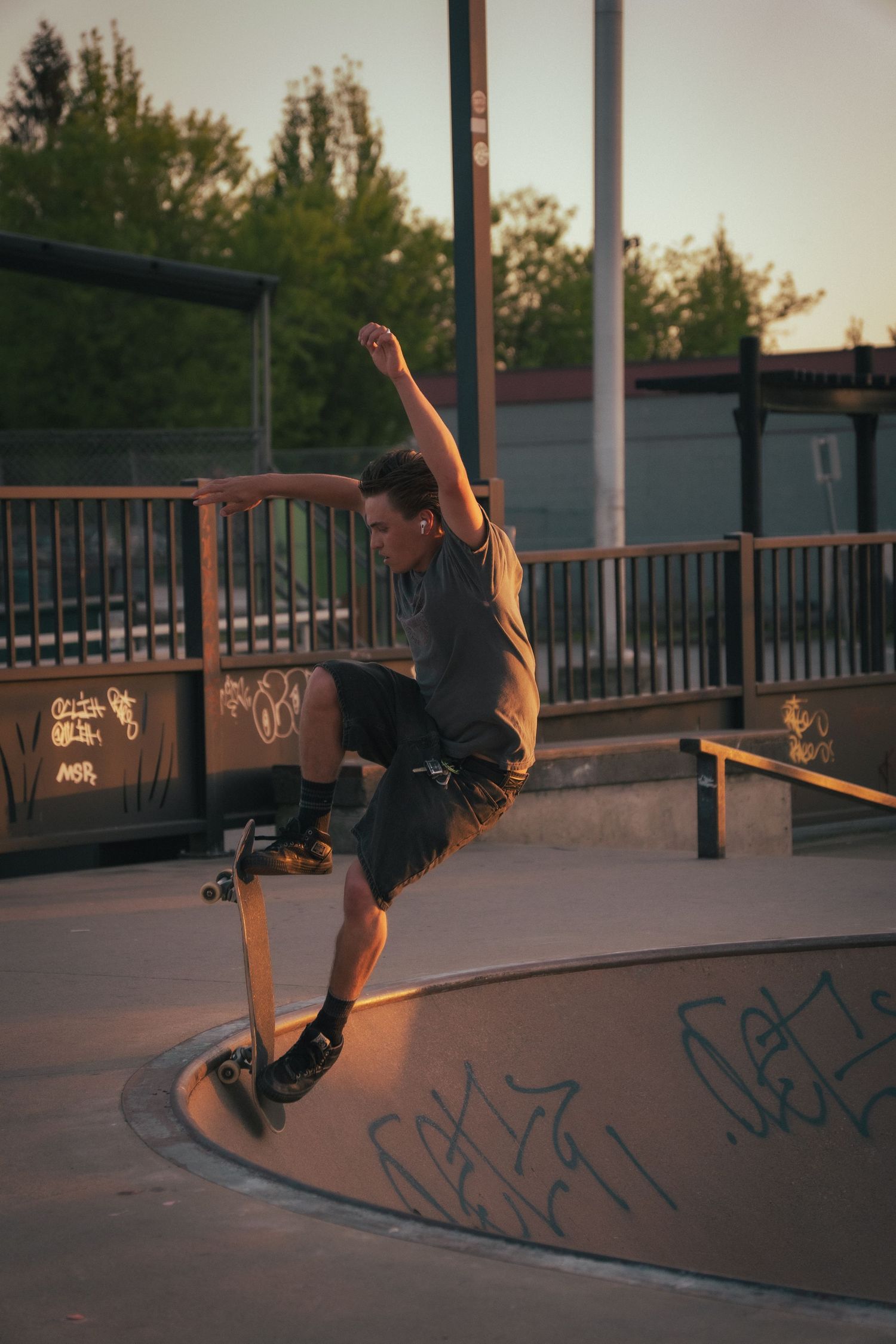Skateboarder performing a trick on the edge of a concrete bowl at sunset in a skate park.