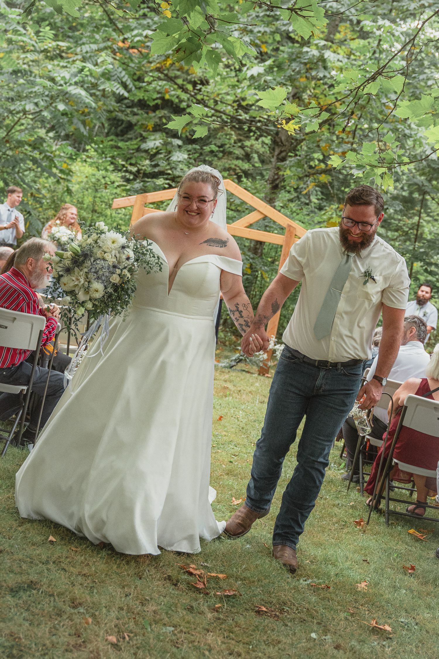 Joyful newlyweds walk back down aisle hand in hand after outdoor garden wedding ceremony.
