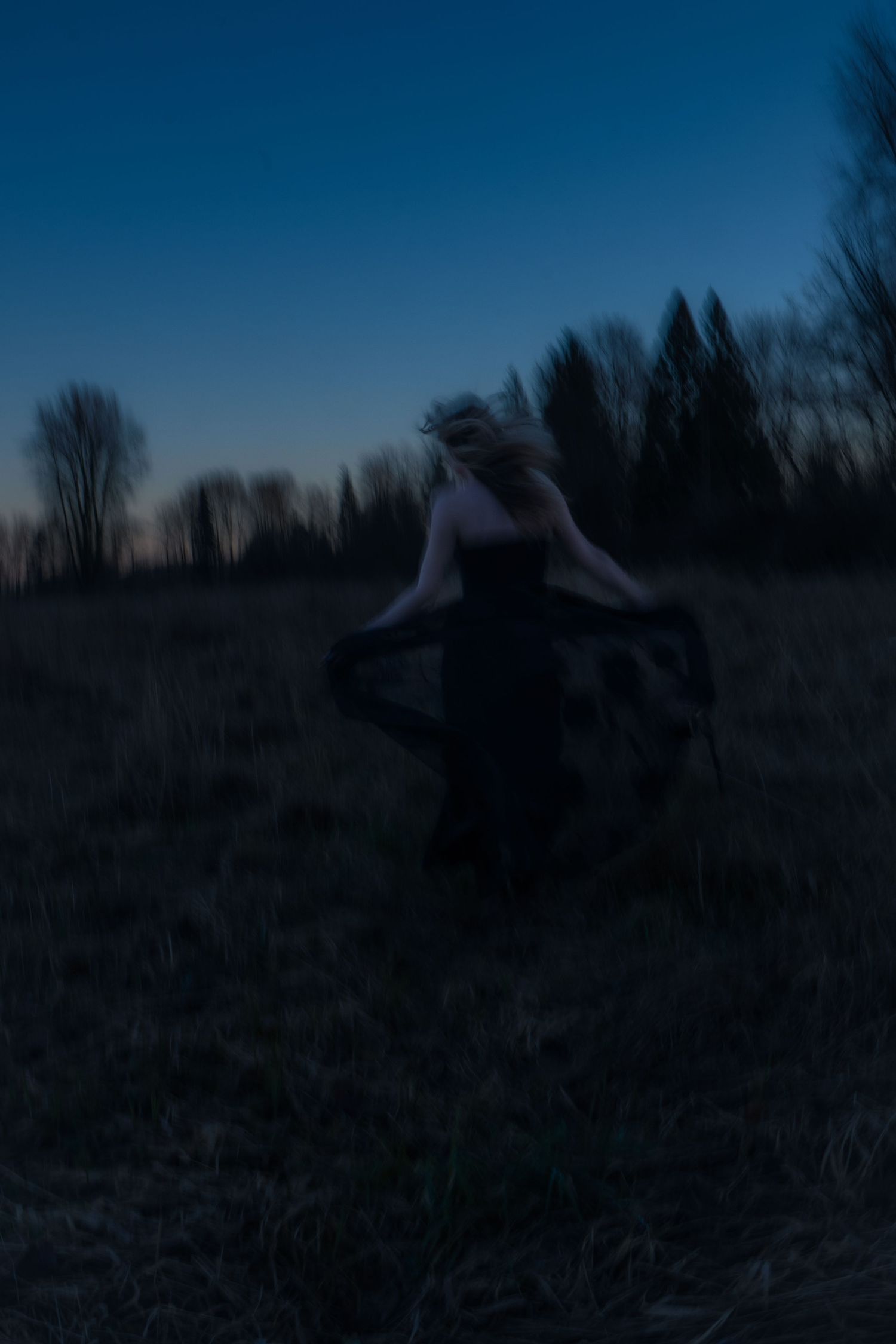 Motion-blurred silhouette of a woman in a black dress dancing in a field at night.