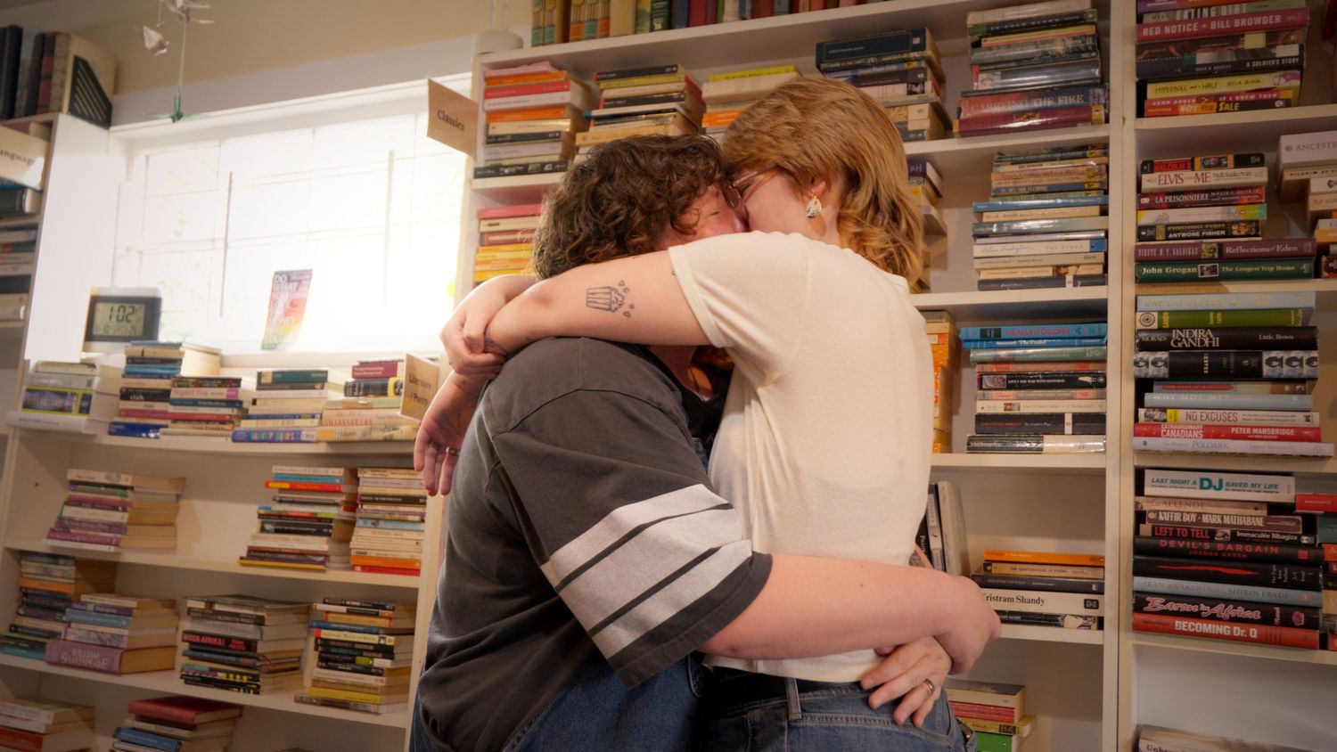 Two people sharing a warm embrace in front of a wall of colorful books.