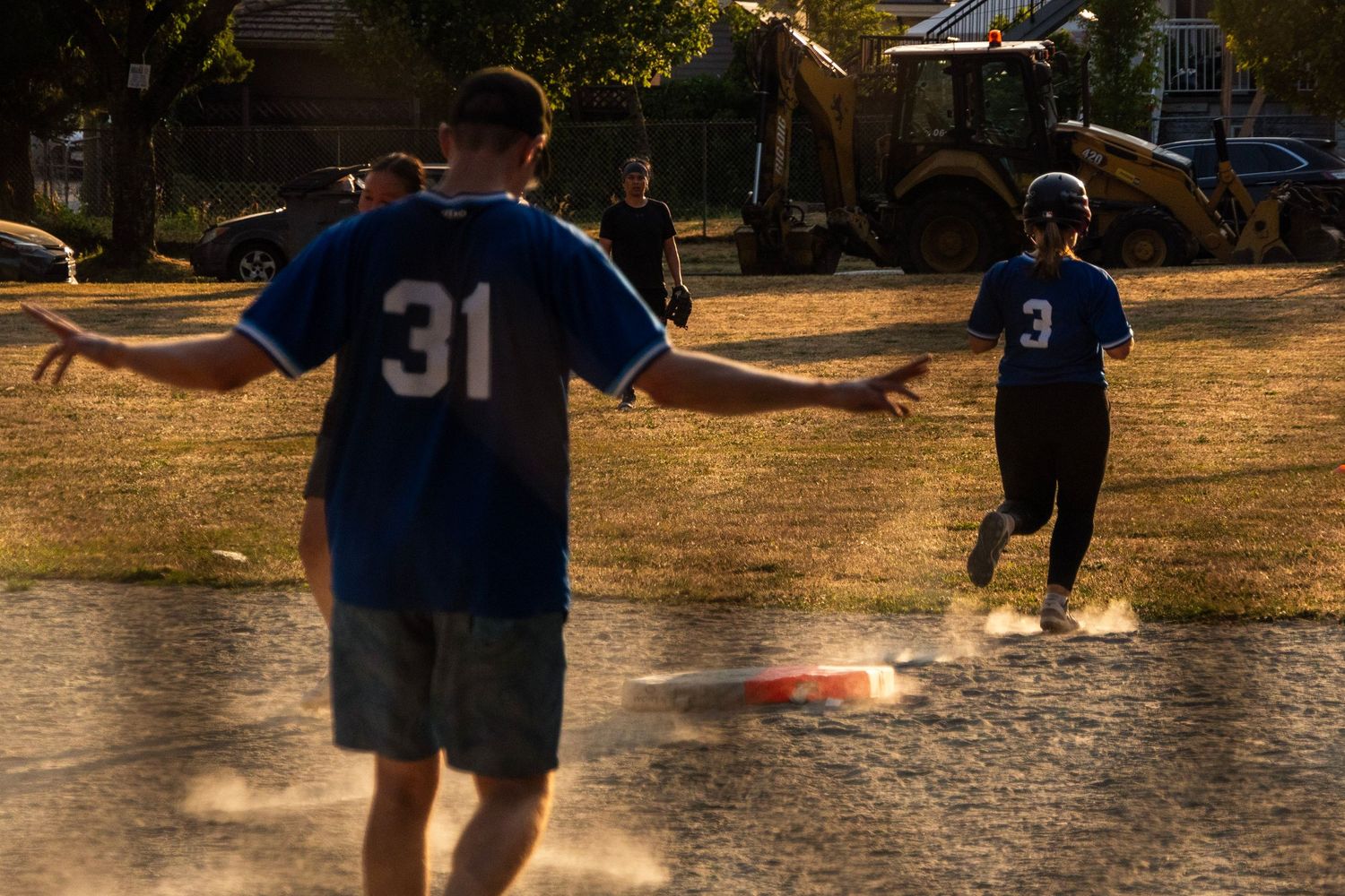 Two softball players in blue jerseys numbered 31 and 3 running bases on a dusty field at sunset.