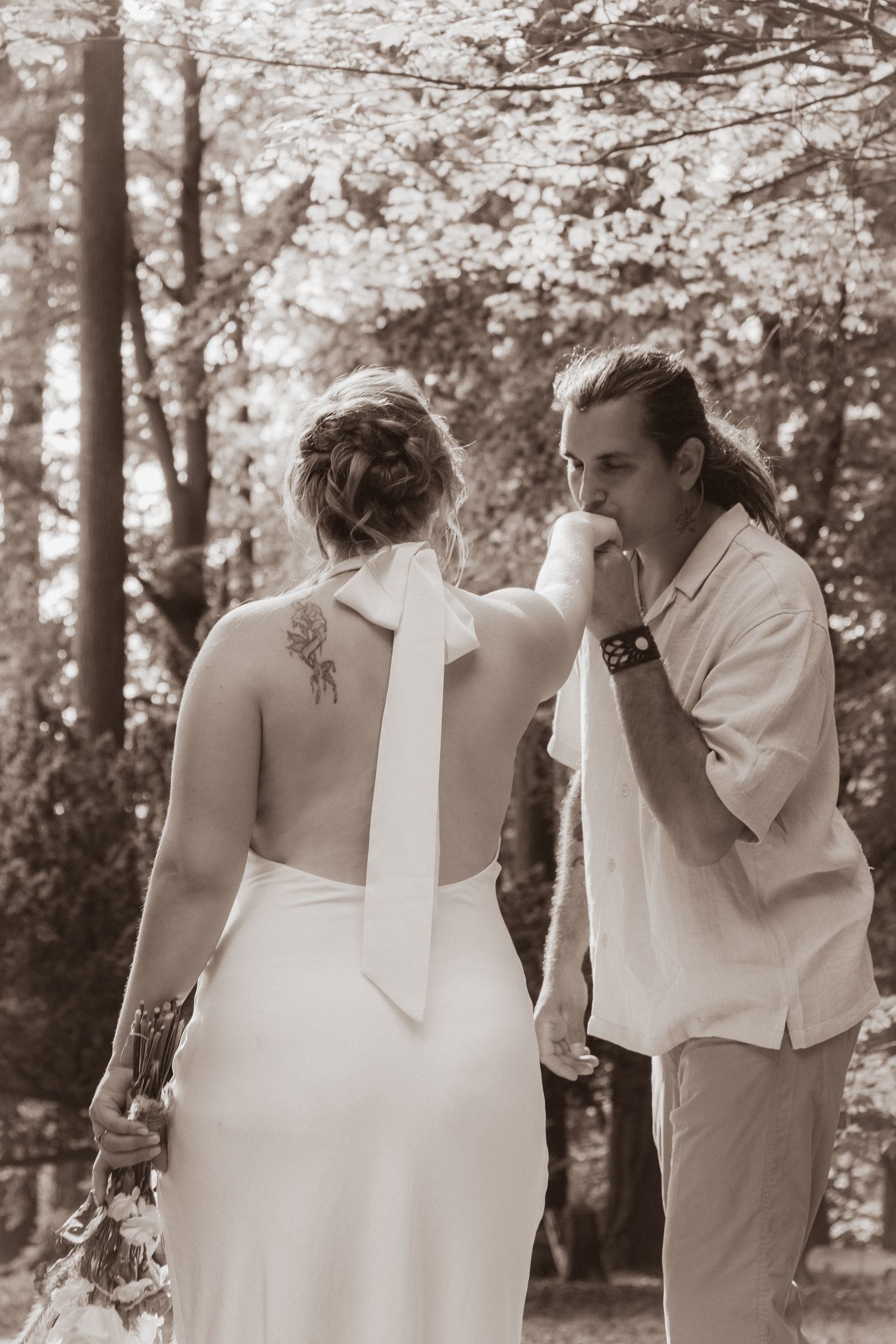 Groom kissing bride's hand in sepia-toned wedding photo with floral backdrop.