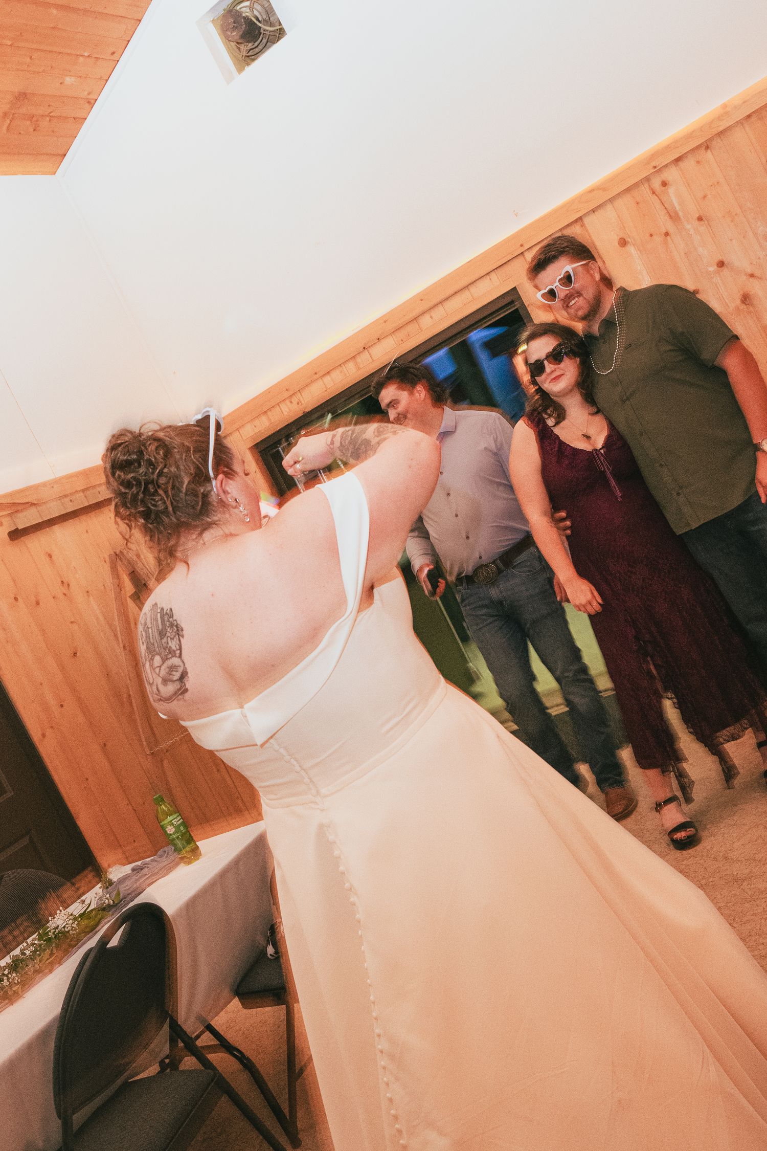 Bride in white wedding gown interacting with guests at rustic reception venue.