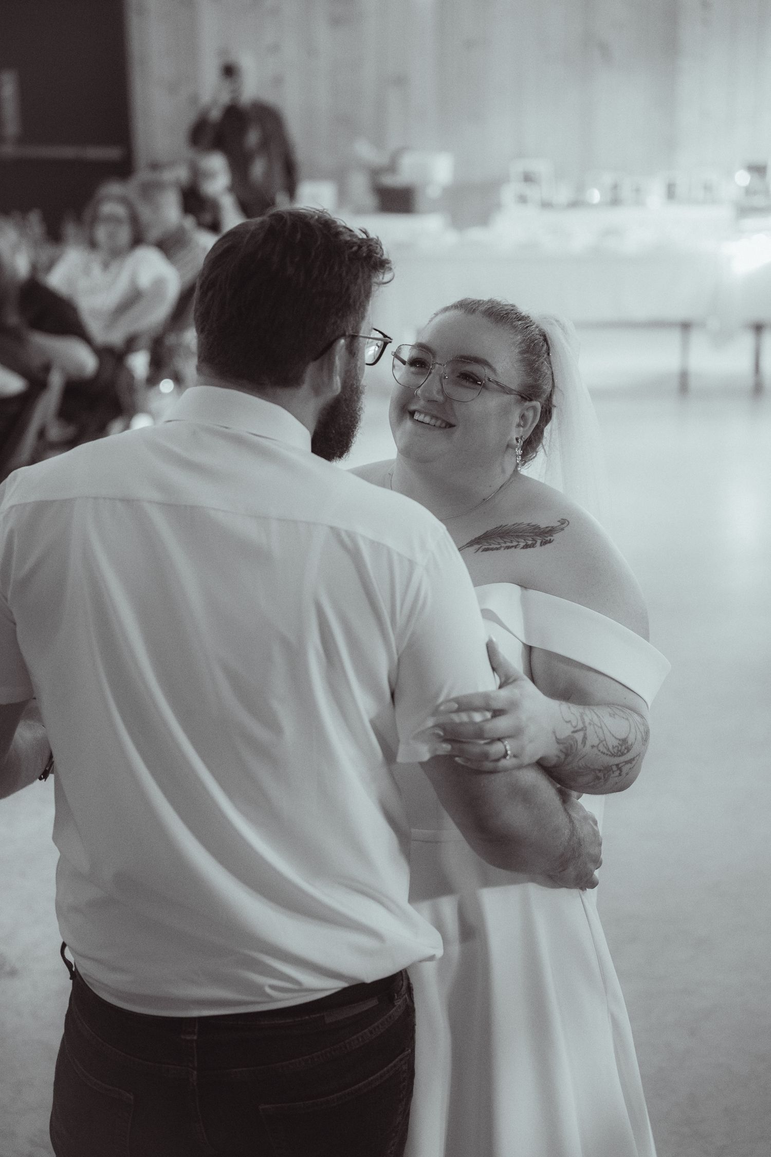Bride and groom share first dance in black and white photo at rustic wedding reception.