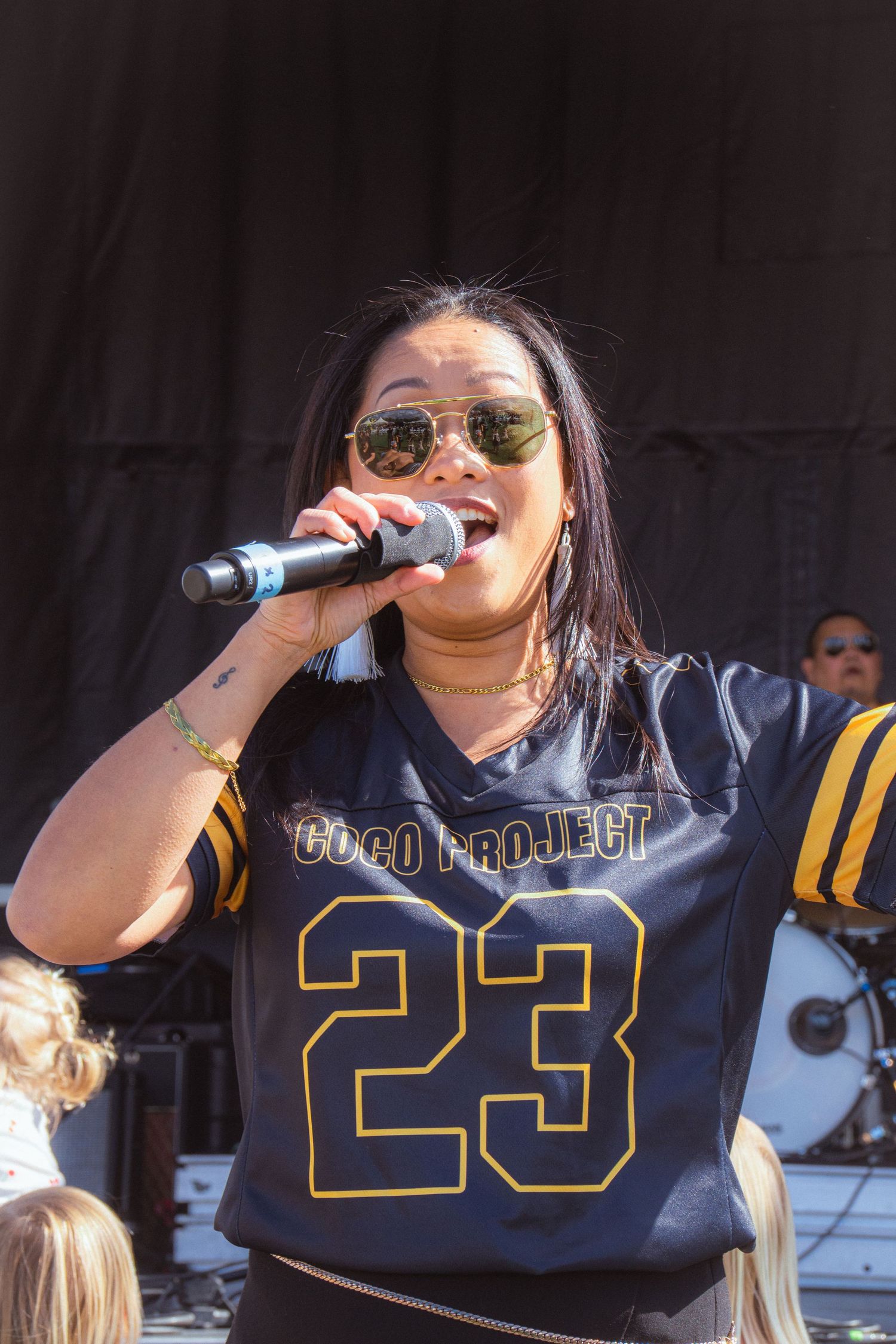 Close-up of female singer in Coco Project number 23 jersey performing with microphone outdoors.