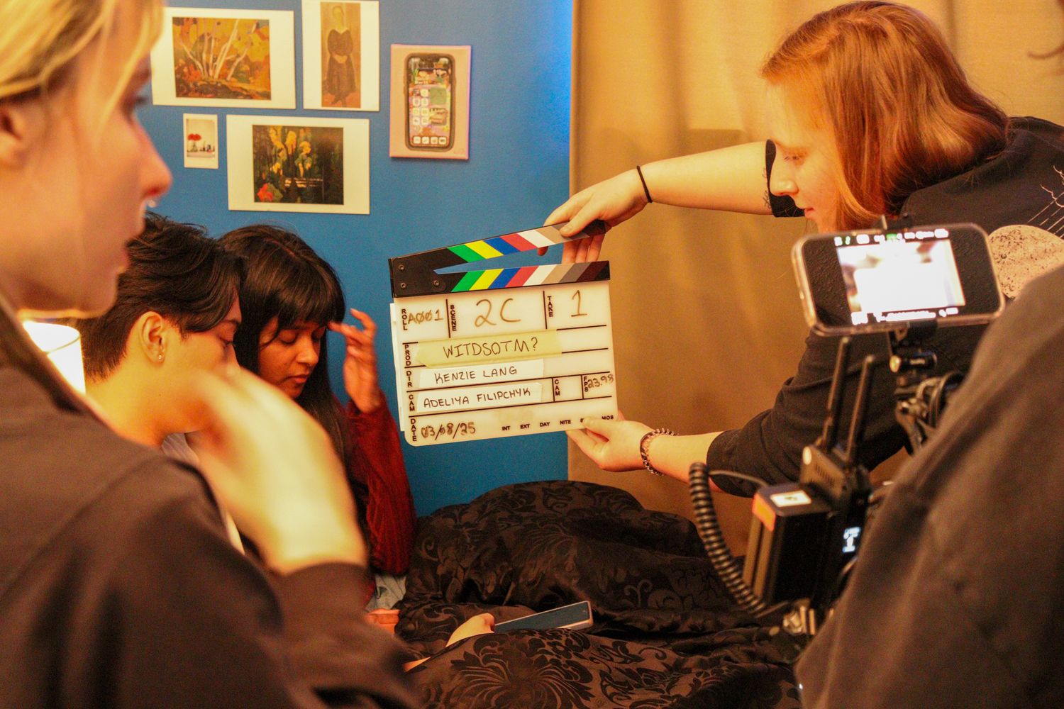Film crew member holds a clapperboard in front of a camera during an indoor movie shoot.