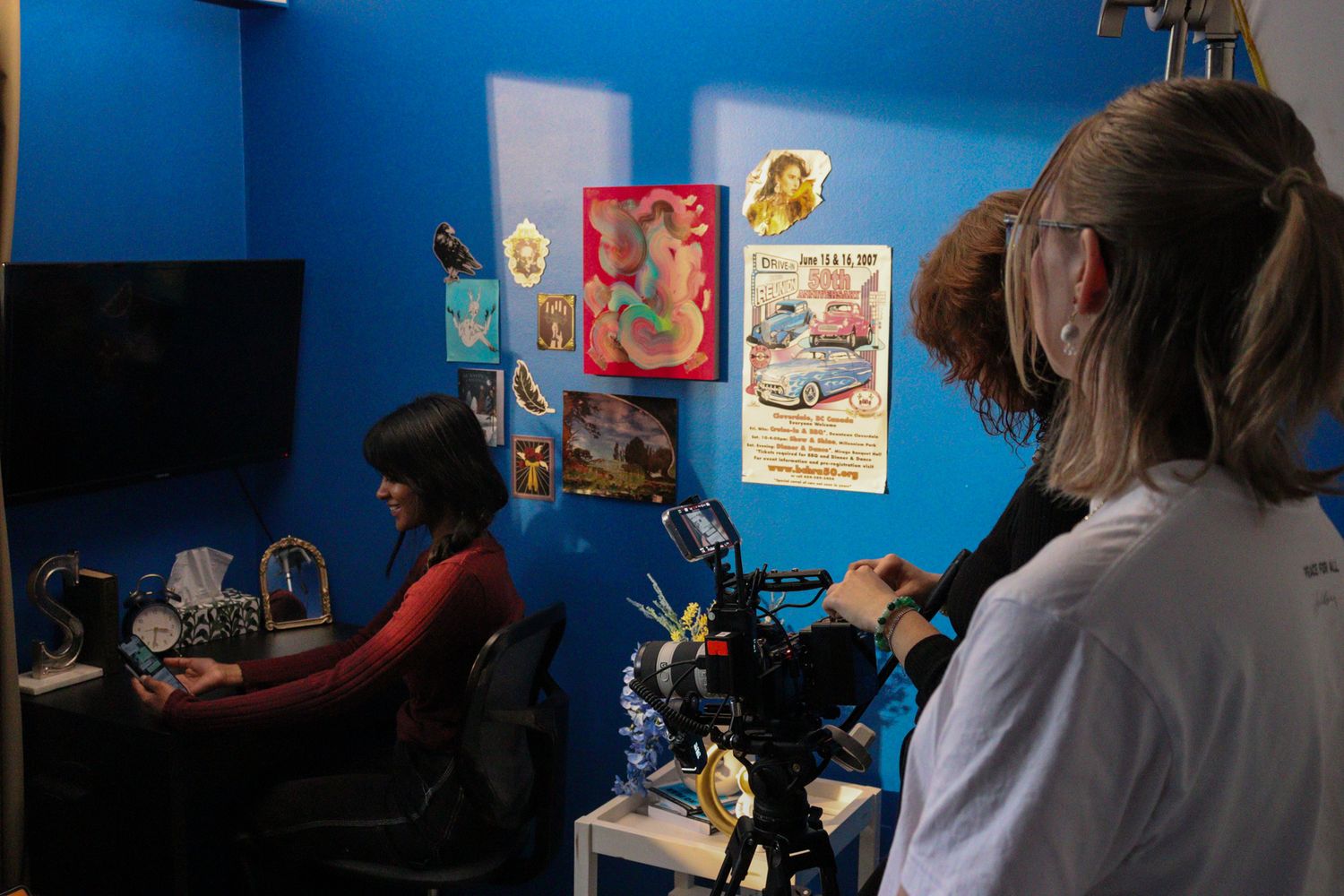 Behind-the-scenes shot of cinematographer filming woman at desk in blue-walled room.