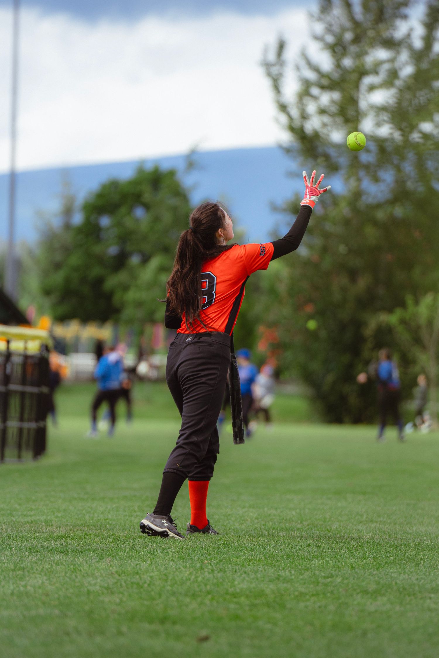 Female softball player #3 in orange jersey catching ball in outfield.
