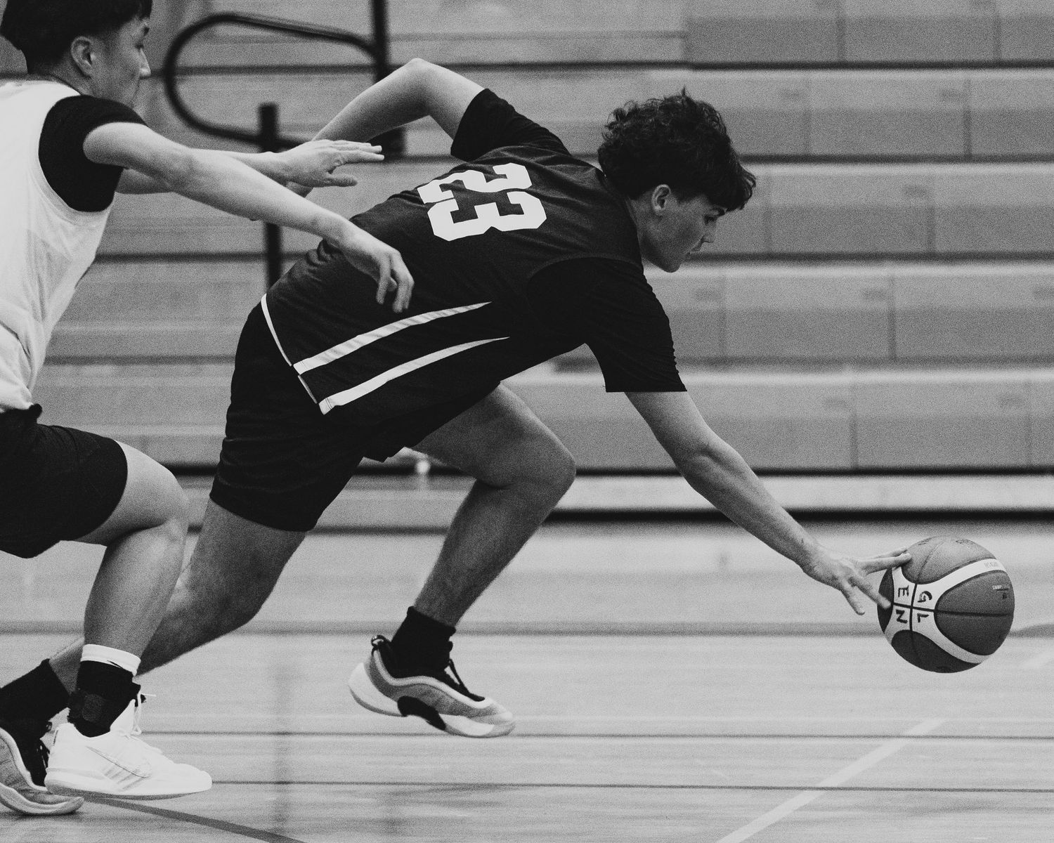Black and white action shot of basketball player #23 in dark jersey diving to save a loose ball on the court.