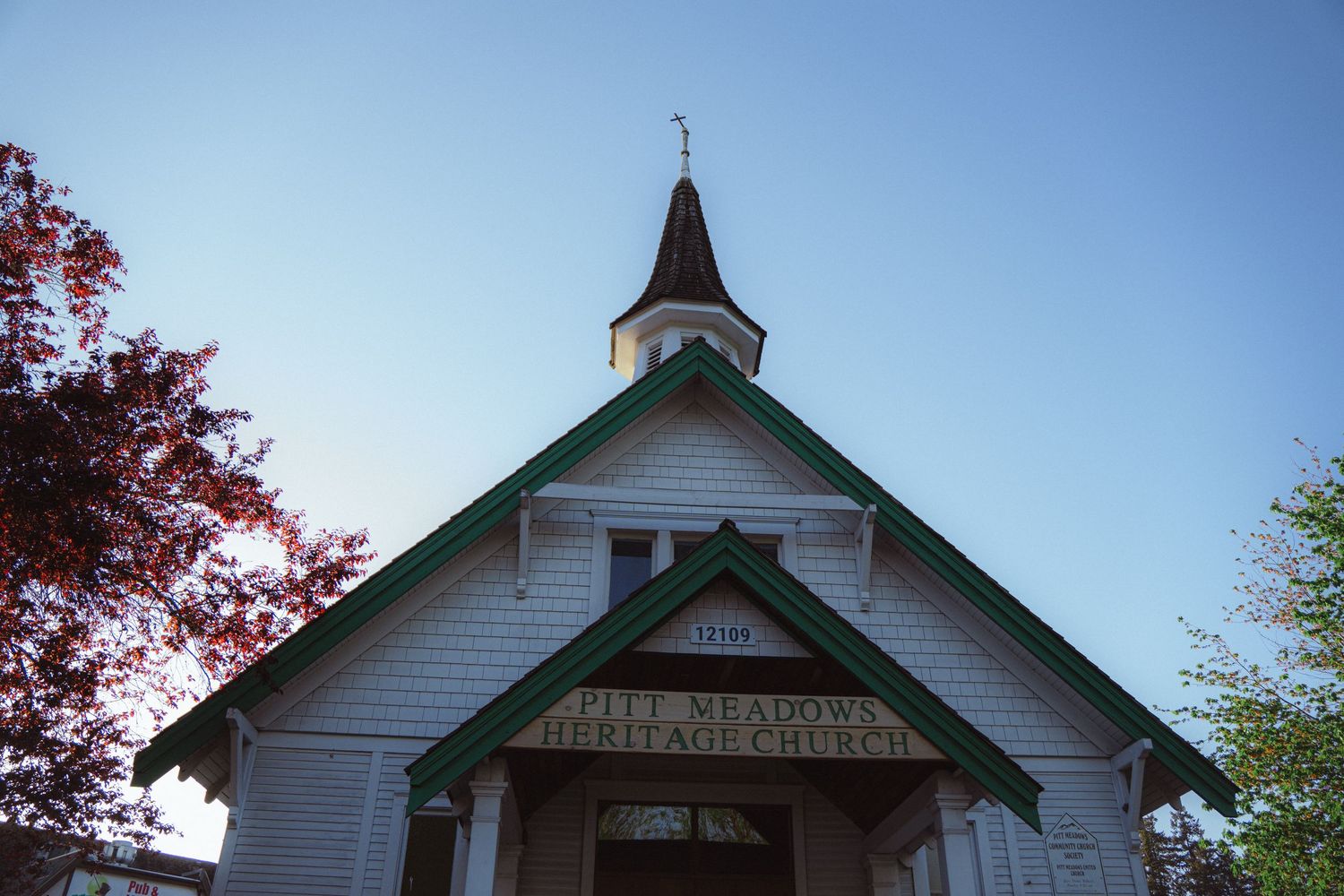 White wooden heritage church with green trim and steeple against a clear blue sky.