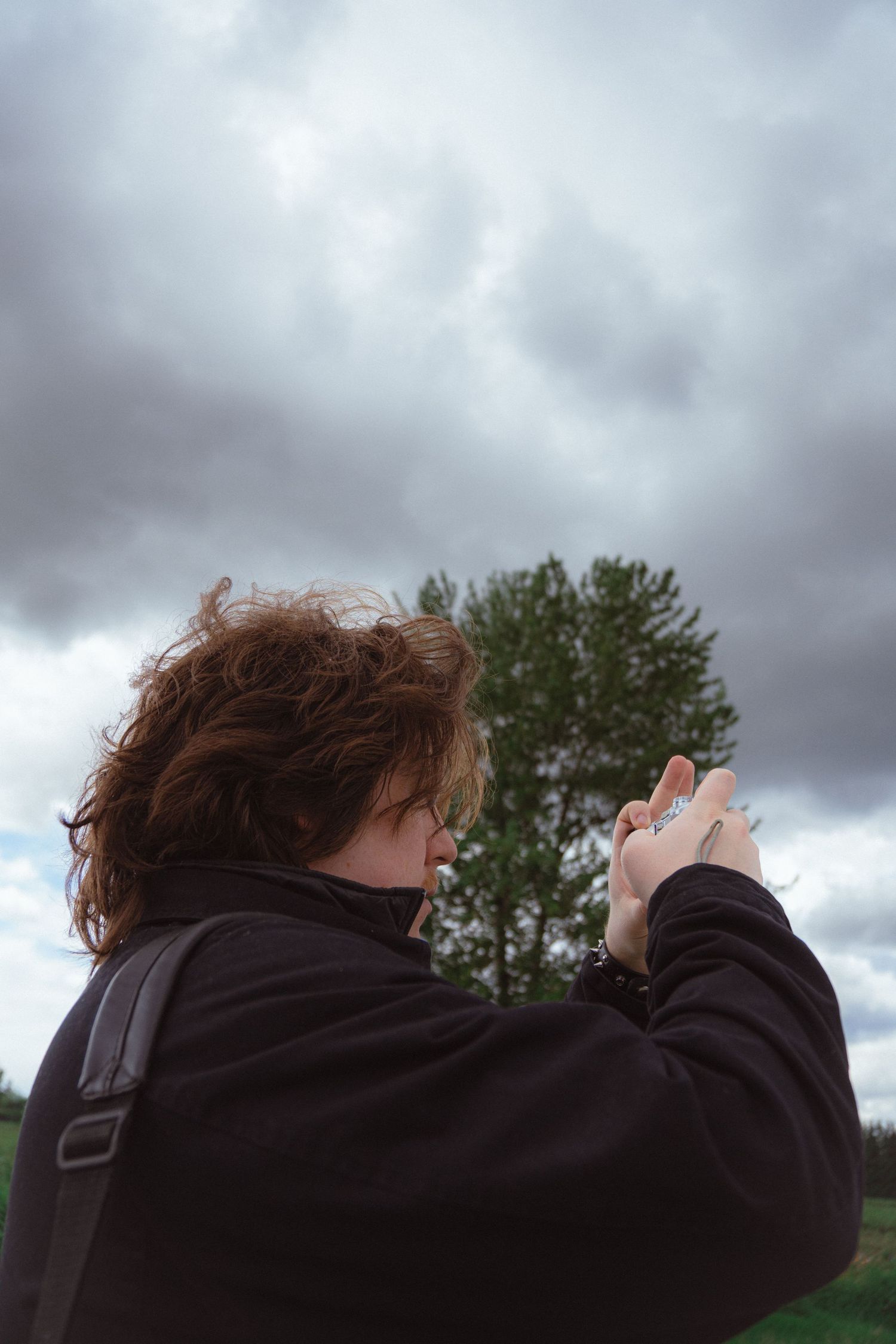 Curly red-haired woman photographing nature with a camera under overcast cloudy skies.