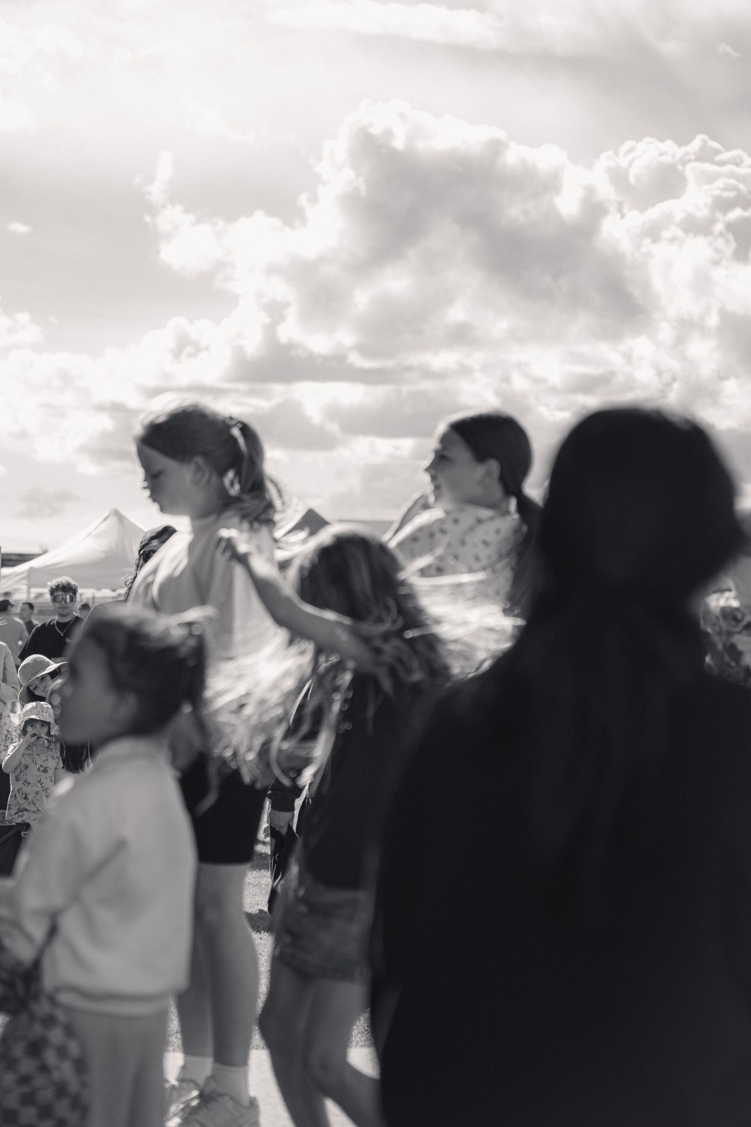 Black and white photo of children dancing at an outdoor music festival under cloudy sky.