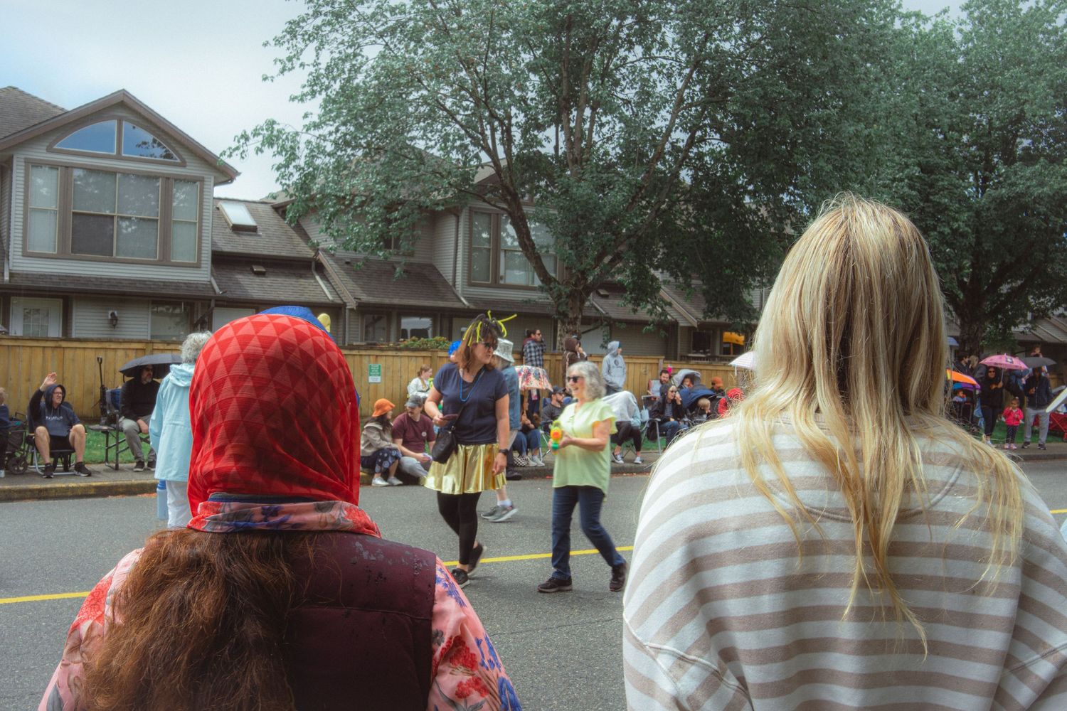 Spectators watch a costumed performer during an outdoor community street parade on a cloudy day.