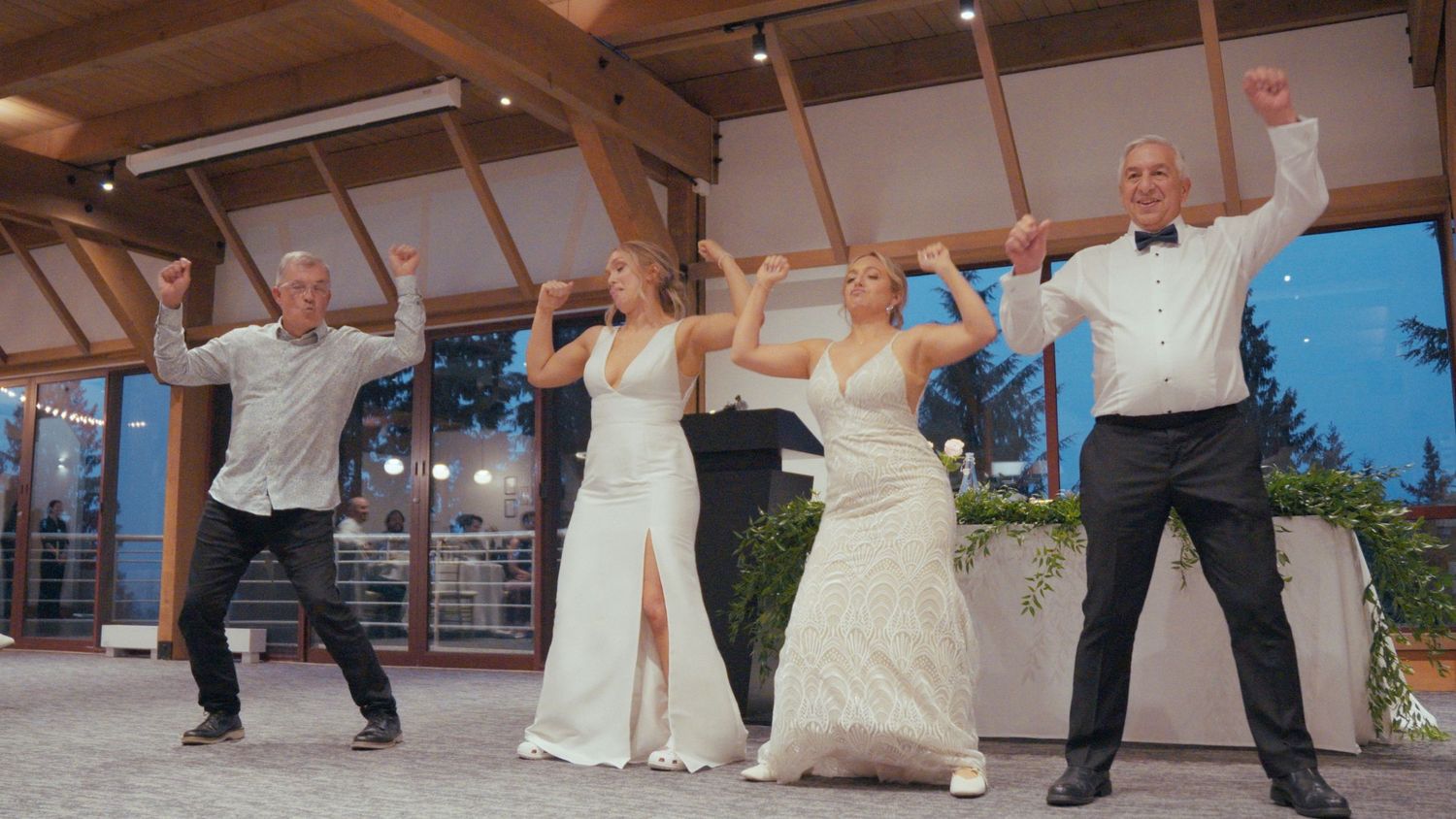 Wedding party performs joyful choreographed dance in elegant venue with string lights at reception.