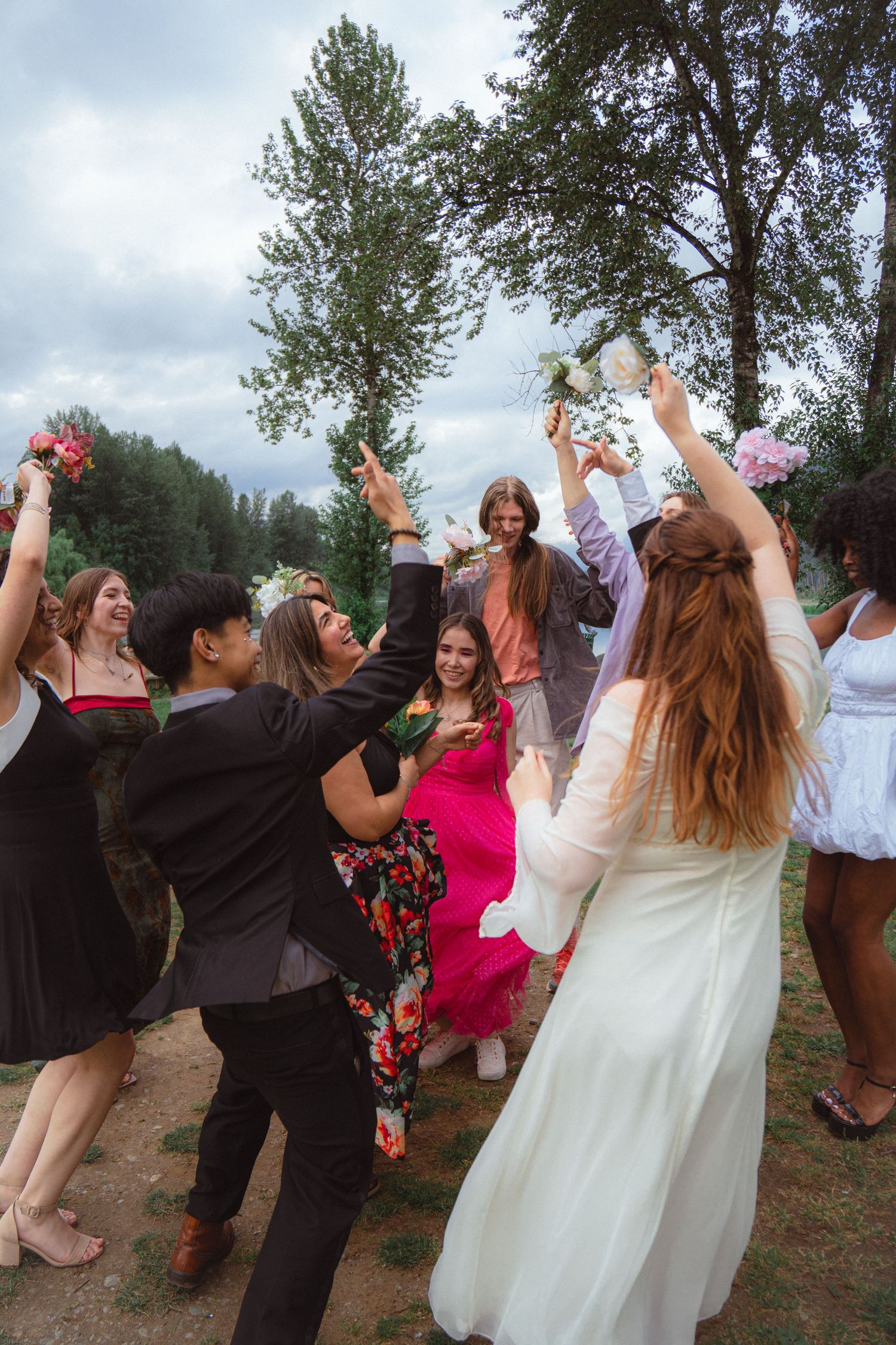 Bride and guests raise flowers in celebration at a lively outdoor wedding party.