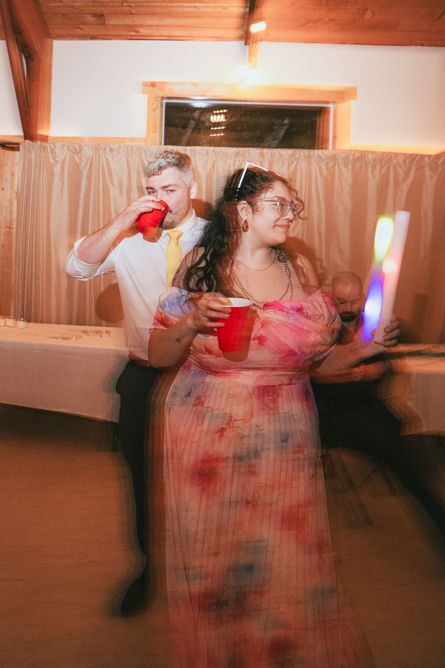Couple dancing and drinking from red solo cups at lively wedding reception party.