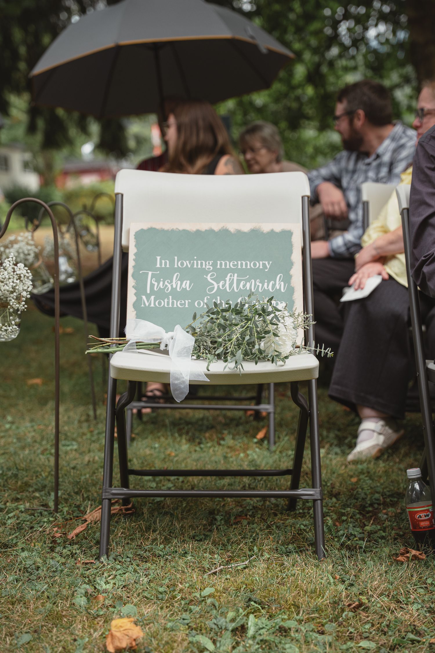 A memorial chair with flowers honors Trisha Settenrich, Mother of the Groom, at an outdoor wedding ceremony.