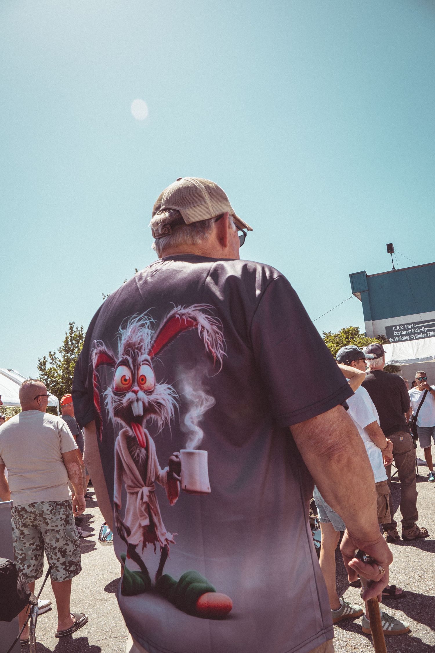 Man wearing funny cartoon character graphic t-shirt at outdoor car show on sunny day.