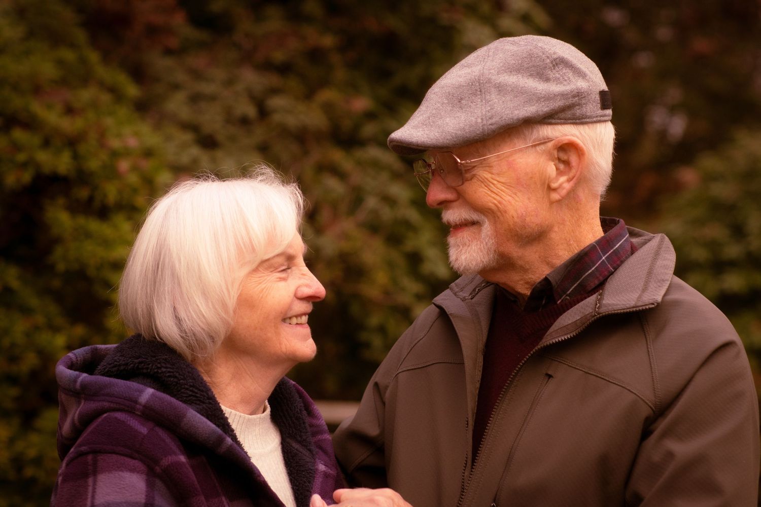 Happy elderly couple gazing at each other lovingly outdoors among fall foliage.