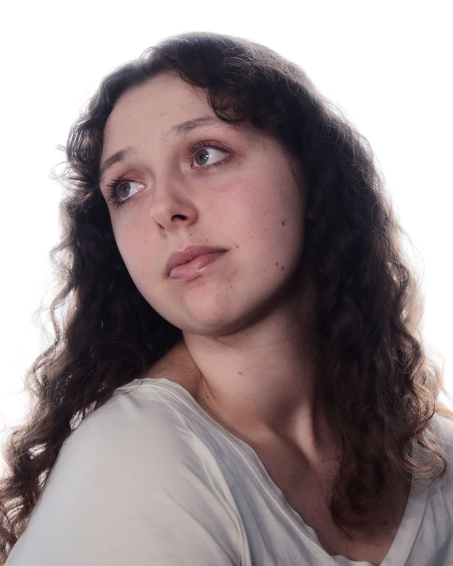 Young woman with long curly dark hair looking upward thoughtfully against a white background.