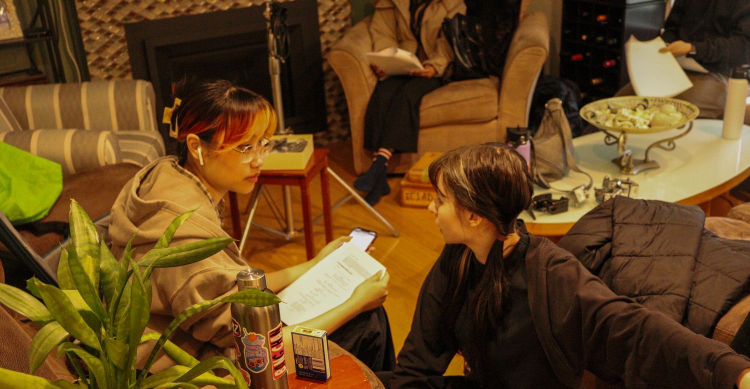 Two actors reviewing a script together in a warmly lit living room on a film set.