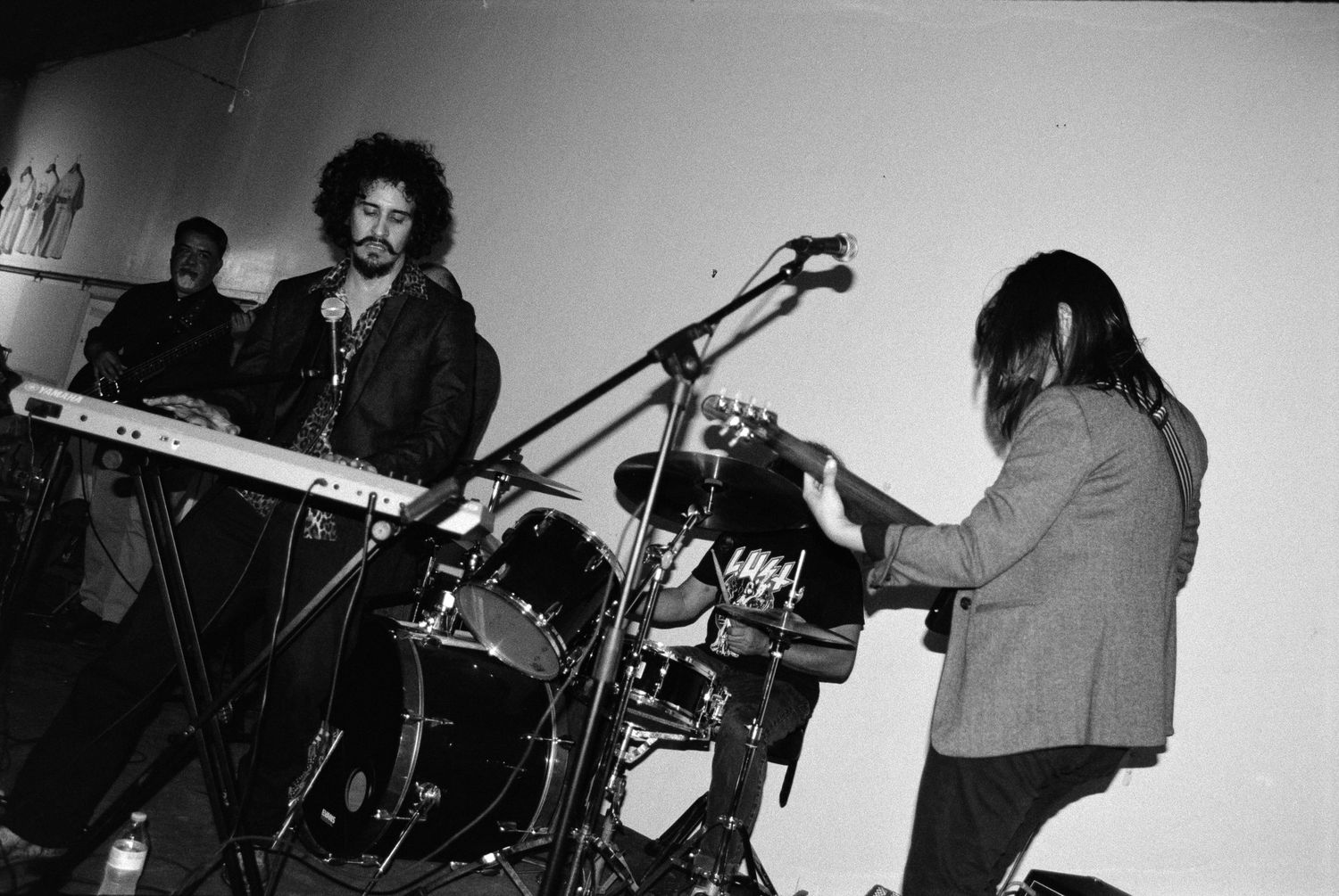 Black and white photo of musicians performing on stage with instruments and equipment.