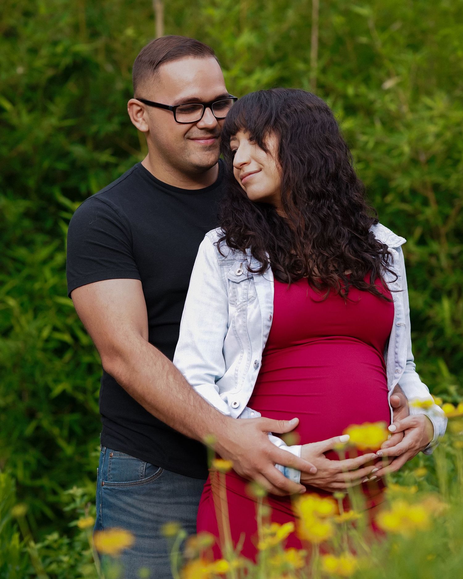 Couple embraces in garden with yellow flowers blooming in background.