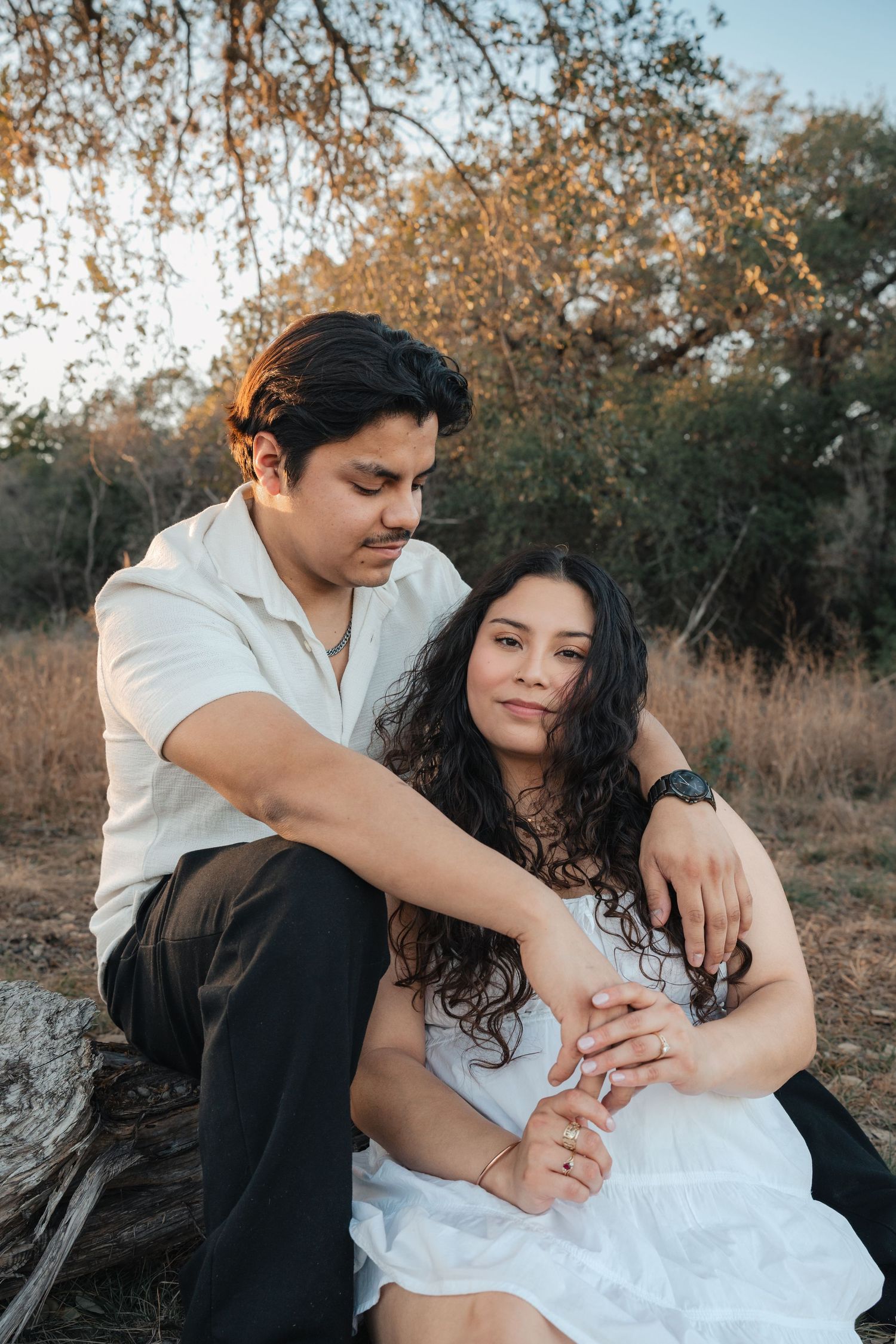 A romantic couple embraces in an outdoor setting with autumn trees and golden light in the background.