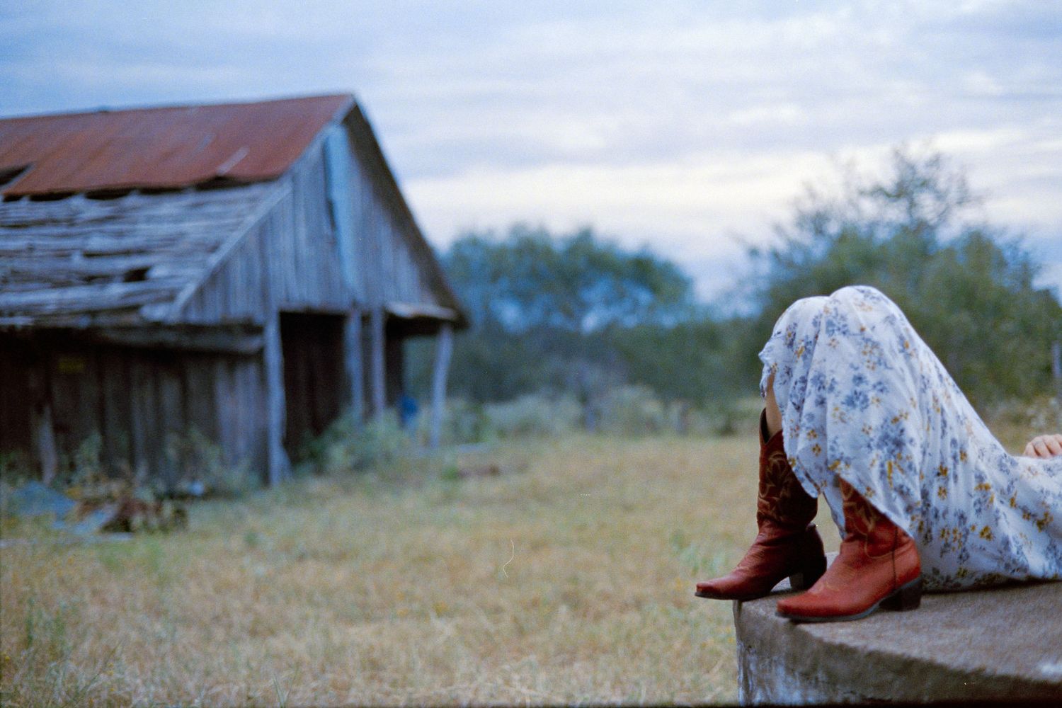 A floral patterned fabric and red shoes rest on a wooden surface near an old barn.