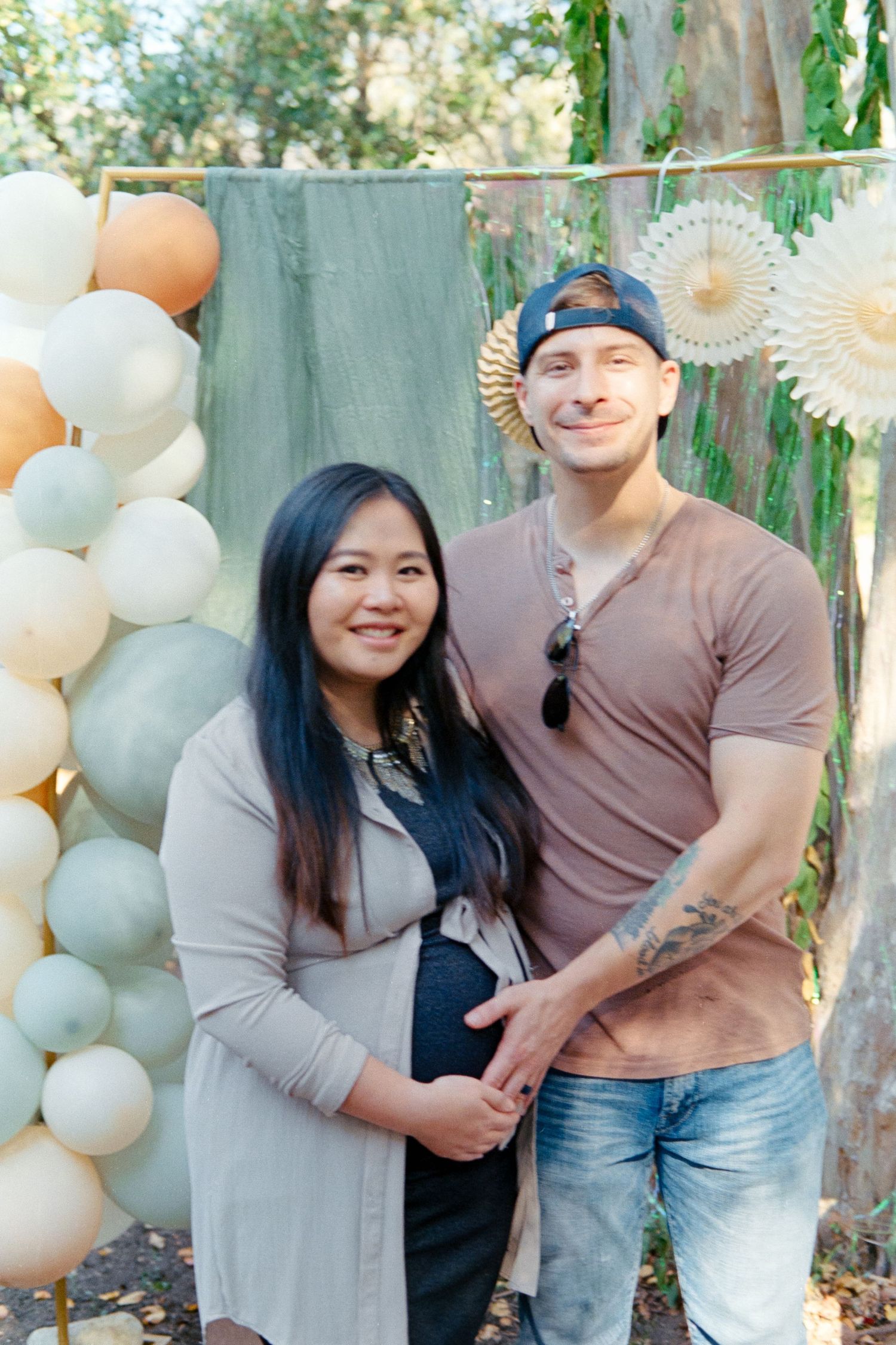 A couple poses together against a backdrop of gray and white balloons in an outdoor setting.