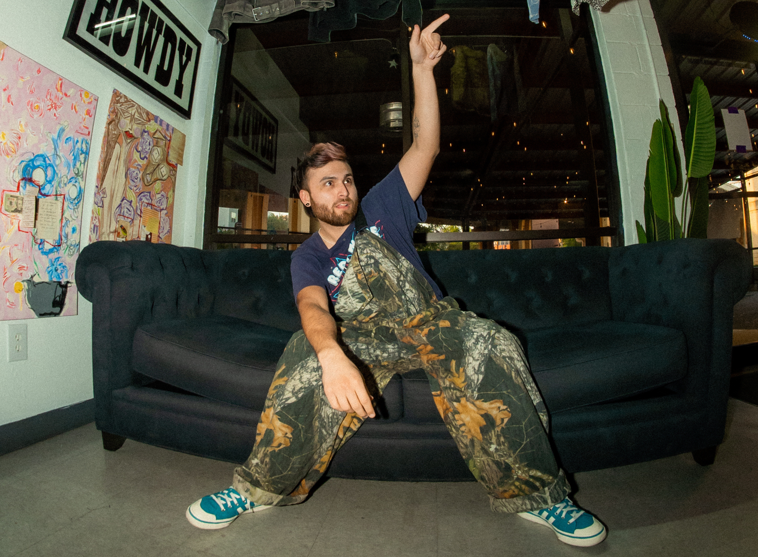 Person in patterned jumpsuit poses dramatically on dark couch.