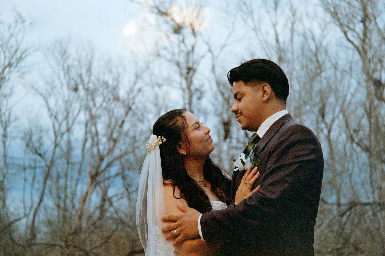 A couple shares an intimate moment outdoors during their wedding ceremony with bare trees in the background.