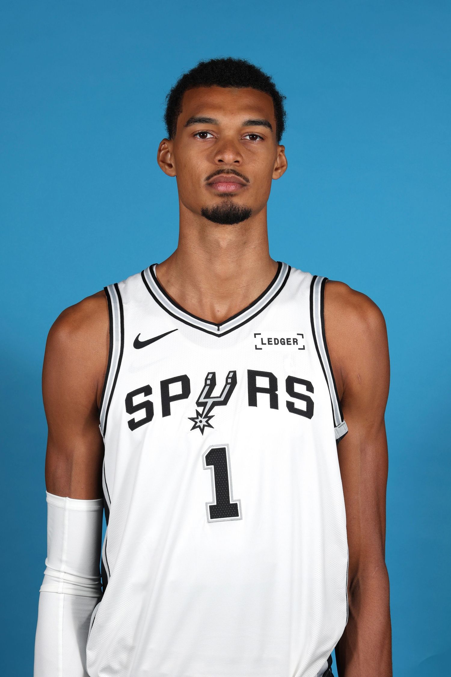 Basketball player wearing white San Antonio Spurs jersey number 1 against blue backdrop.