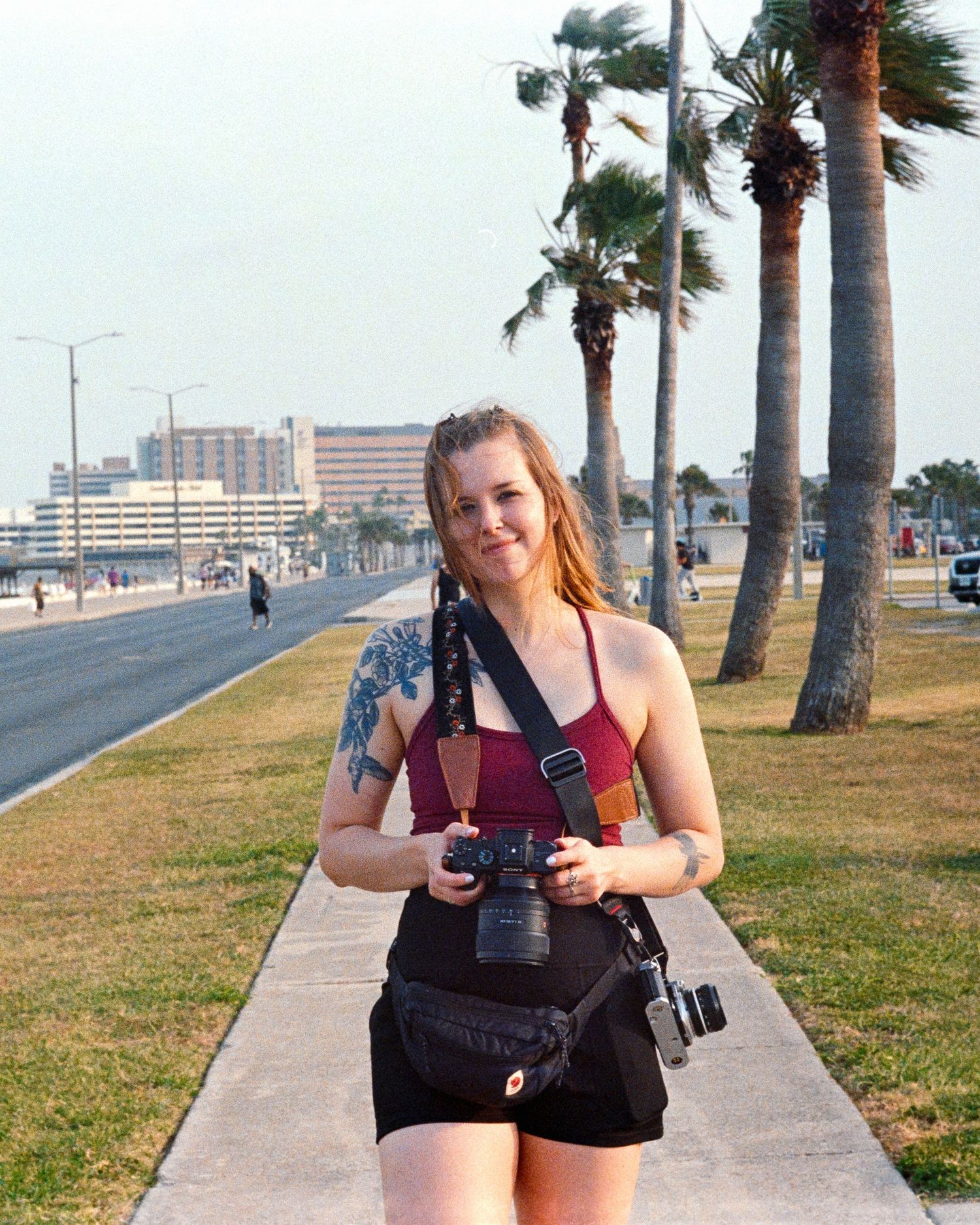 Palm tree lined walkway with someone taking photos on a sunny beach boardwalk.